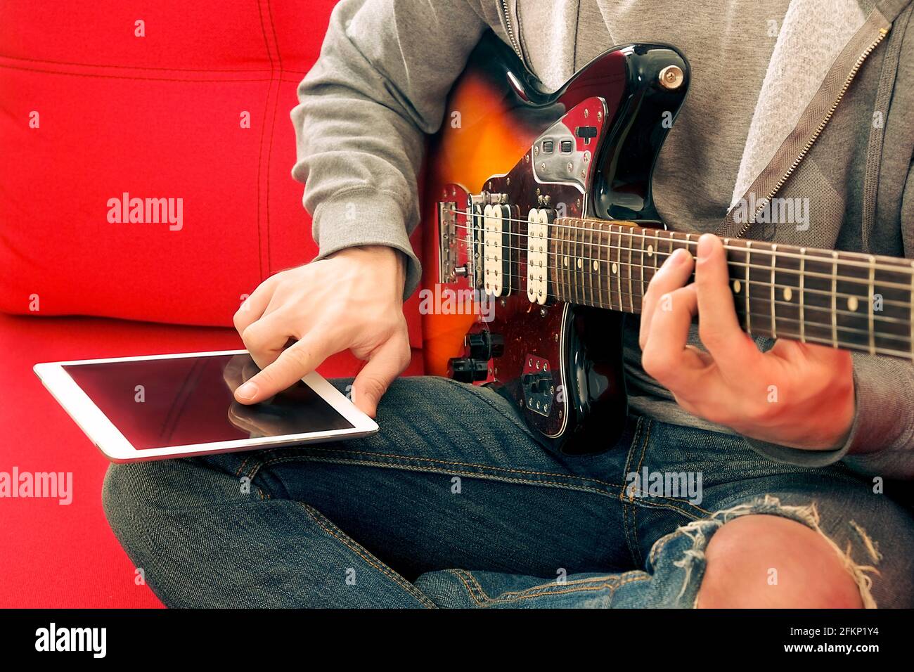 Casual young man in ripped jeans, playing sunburst offset electric