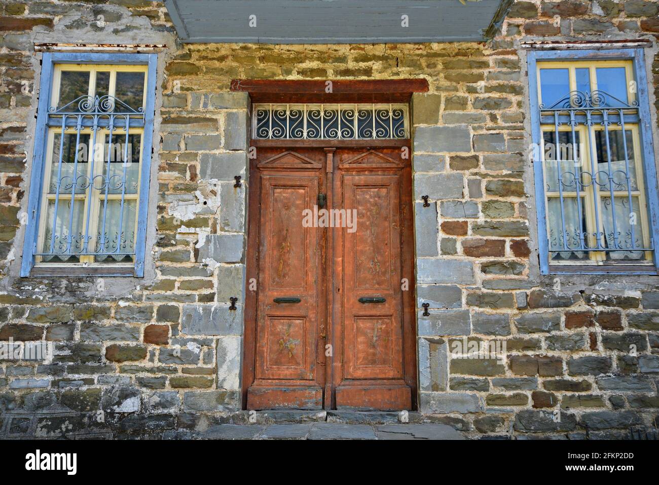 Rural stone house facade with a weathered wooden door and windows with ...