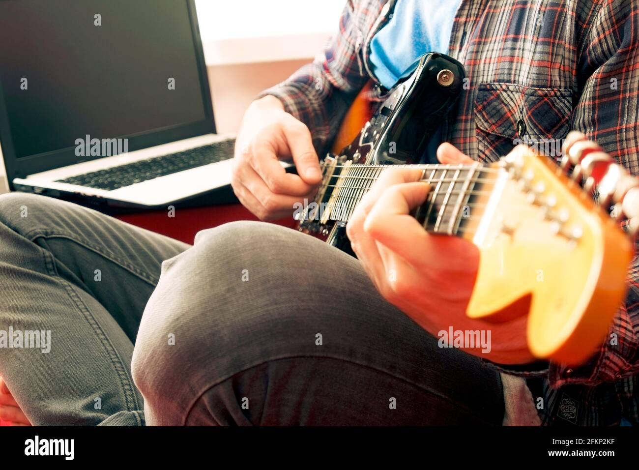 Young man, hipster folk singer songwriter in checkered plaid shirt, playing sunburst offset electric guitar. Male guitarist taking online jazz music c Stock Photo