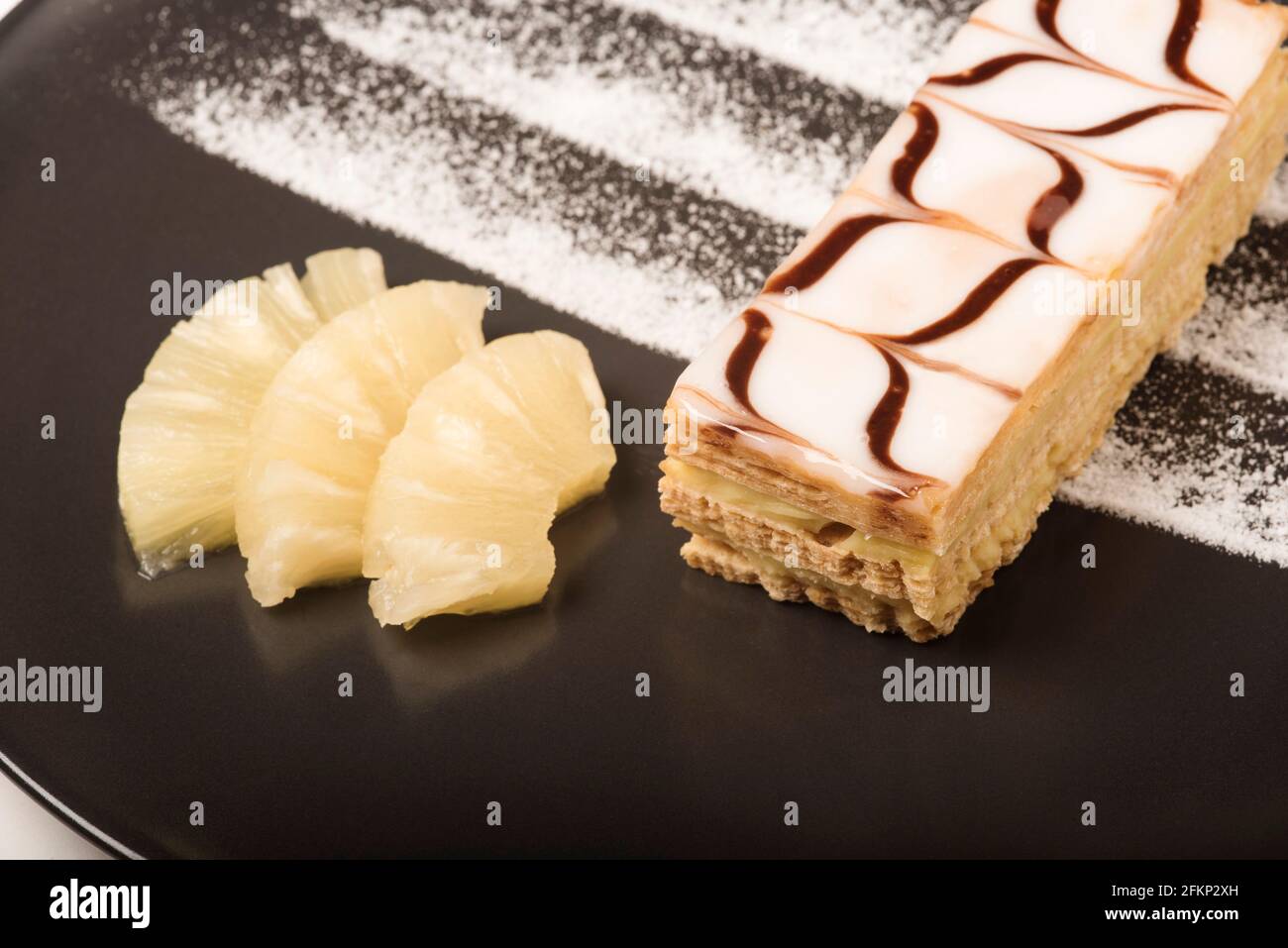 Nouvelle cuisine style presentation of a Millefeuille pastry aka vanilla slice or custard slice served with pineapple. Stock Photo