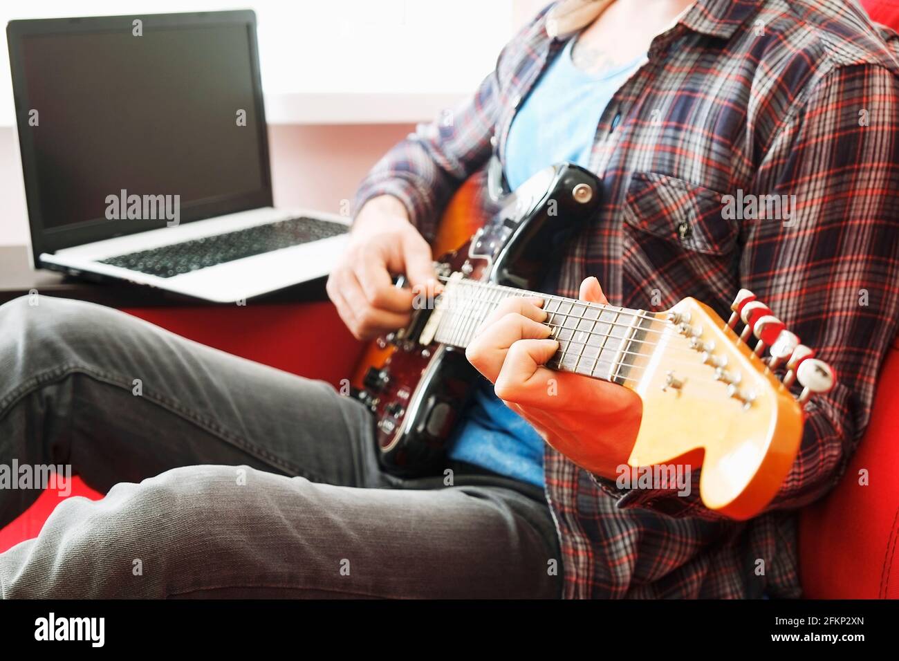 Young man, hipster folk singer songwriter in checkered plaid shirt, playing sunburst offset electric guitar. Male guitarist taking online jazz music c Stock Photo