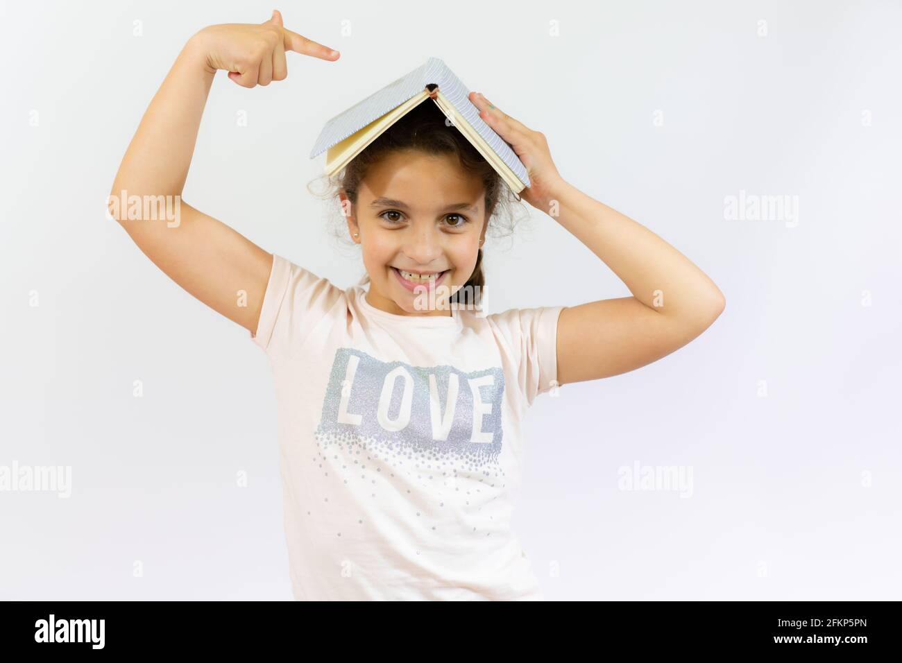 Lovely little girl standing and holding a book over white background ...