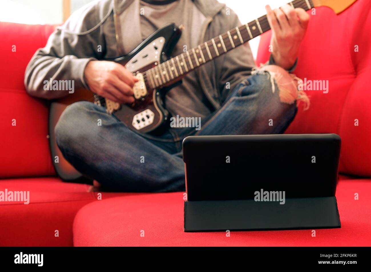 Casual young man in ripped jeans, playing sunburst offset electric guitar. Young musician taking online musical instrument course lesson on wireless i Stock Photo