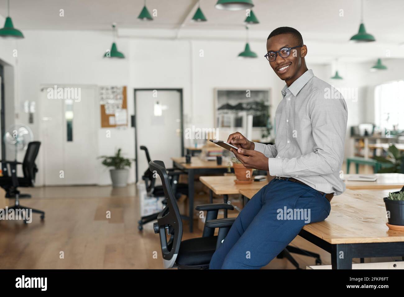African businessman smiling while using a tablet at his office desk Stock Photo