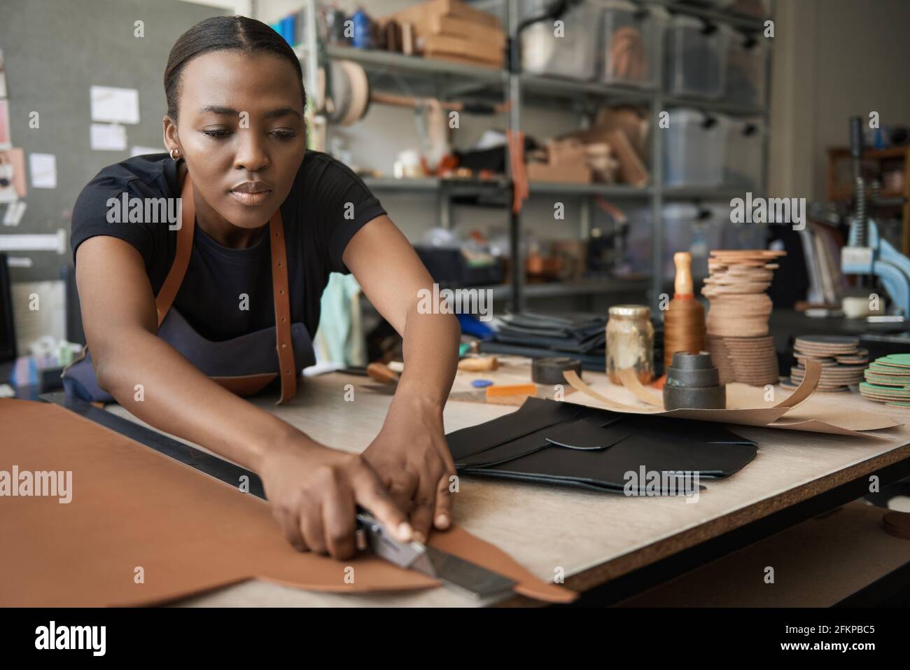 Young African female leather worker cutting leather at a bench Stock Photo