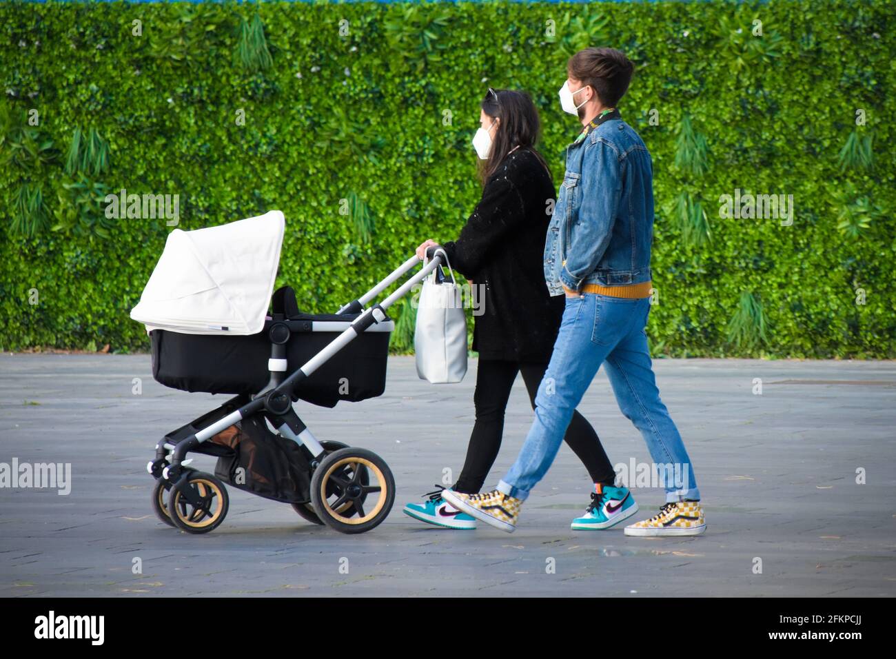 Couple with mask walking down a street with their baby stroller during coronavirus pandemic. Stock Photo