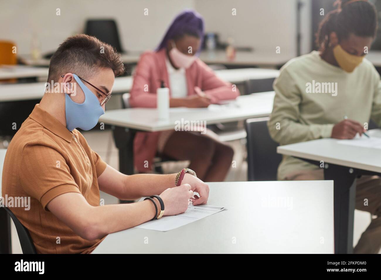 Side view portrait of young man wearing mask while taking test or exam in school with diverse group of people, copy space Stock Photo