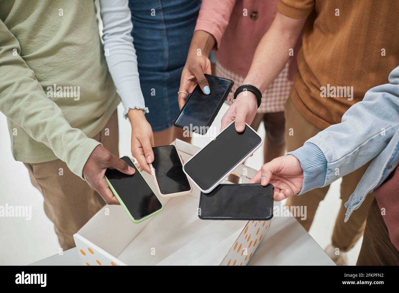 Top view closeup of diverse group of teenagers putting smartphones in box in no gadget classroom at school, copy space Stock Photo