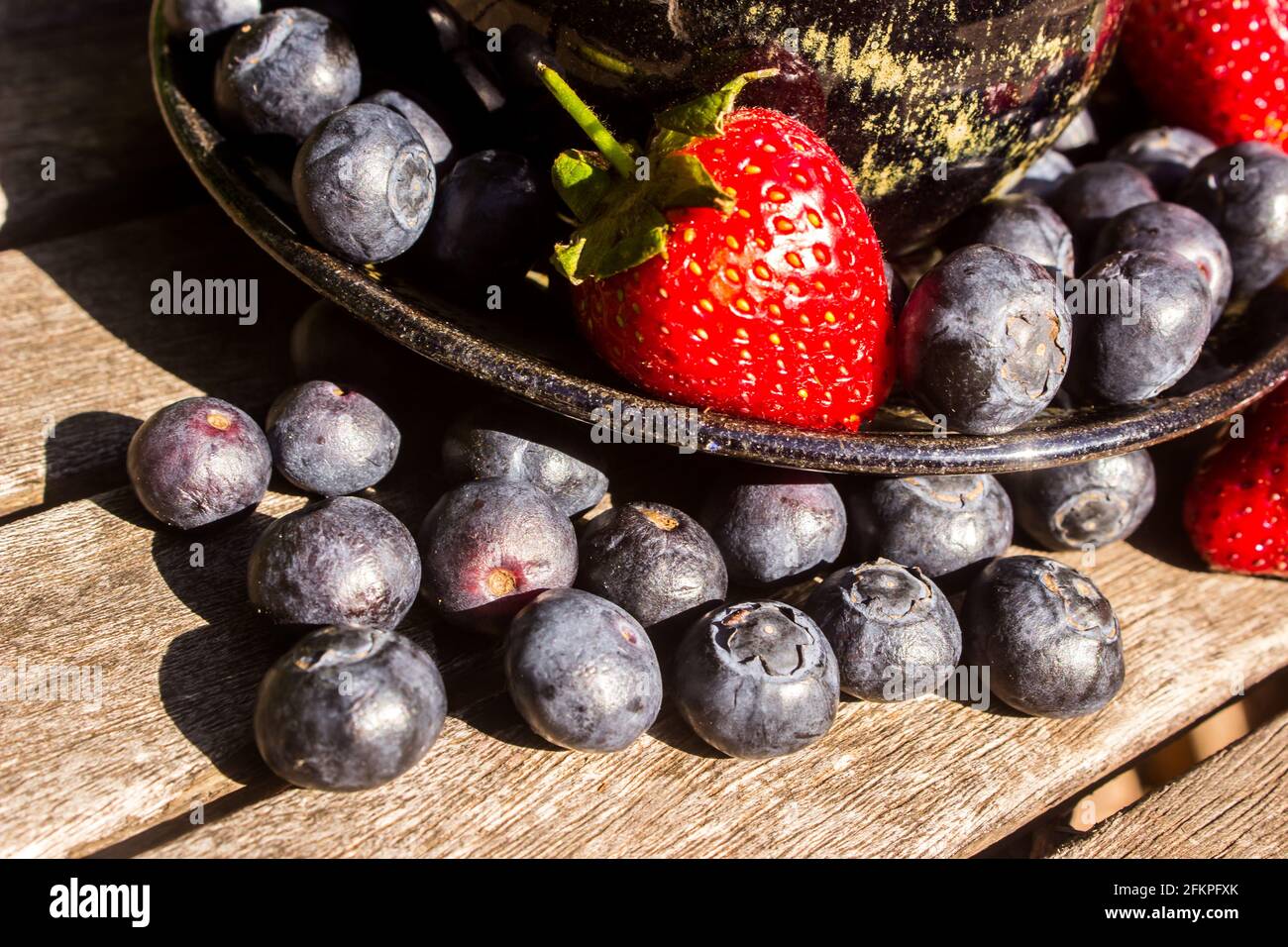 Blue berries on a weathered wooden tabletop in front of a saucer filled with both blueberries and strawberries Stock Photo