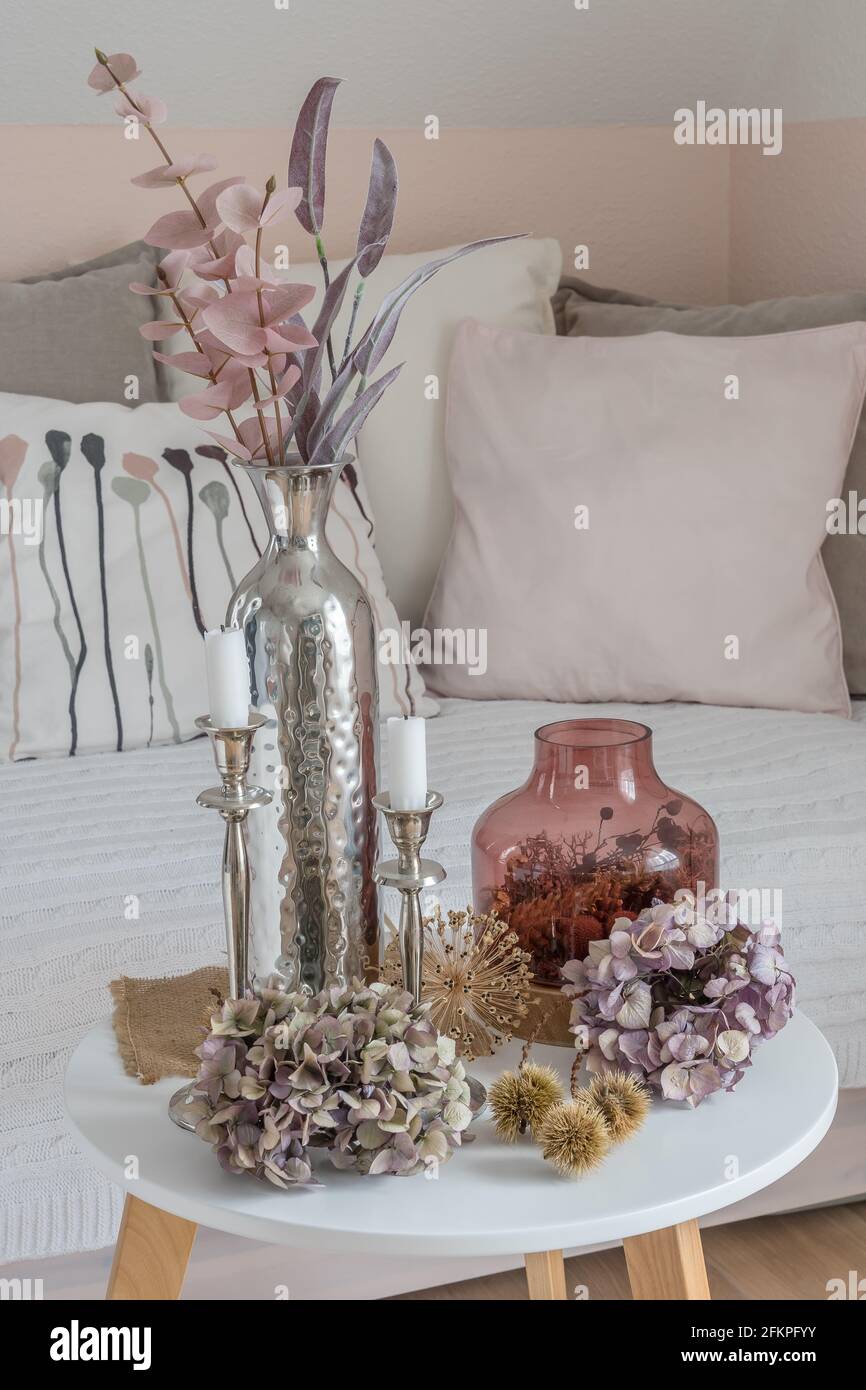 Beautiful harmonious autumn decoration on coffee table with dried hydrangea flowers, chestnut bowls, pink glass vase, pink and purple branches and whi Stock Photo