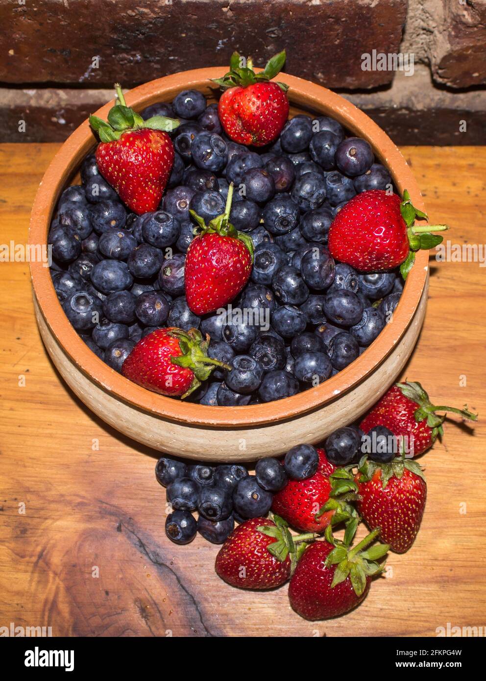 A pottery bowl, filled to overflowing with fresh blueberries and Strawberries Stock Photo
