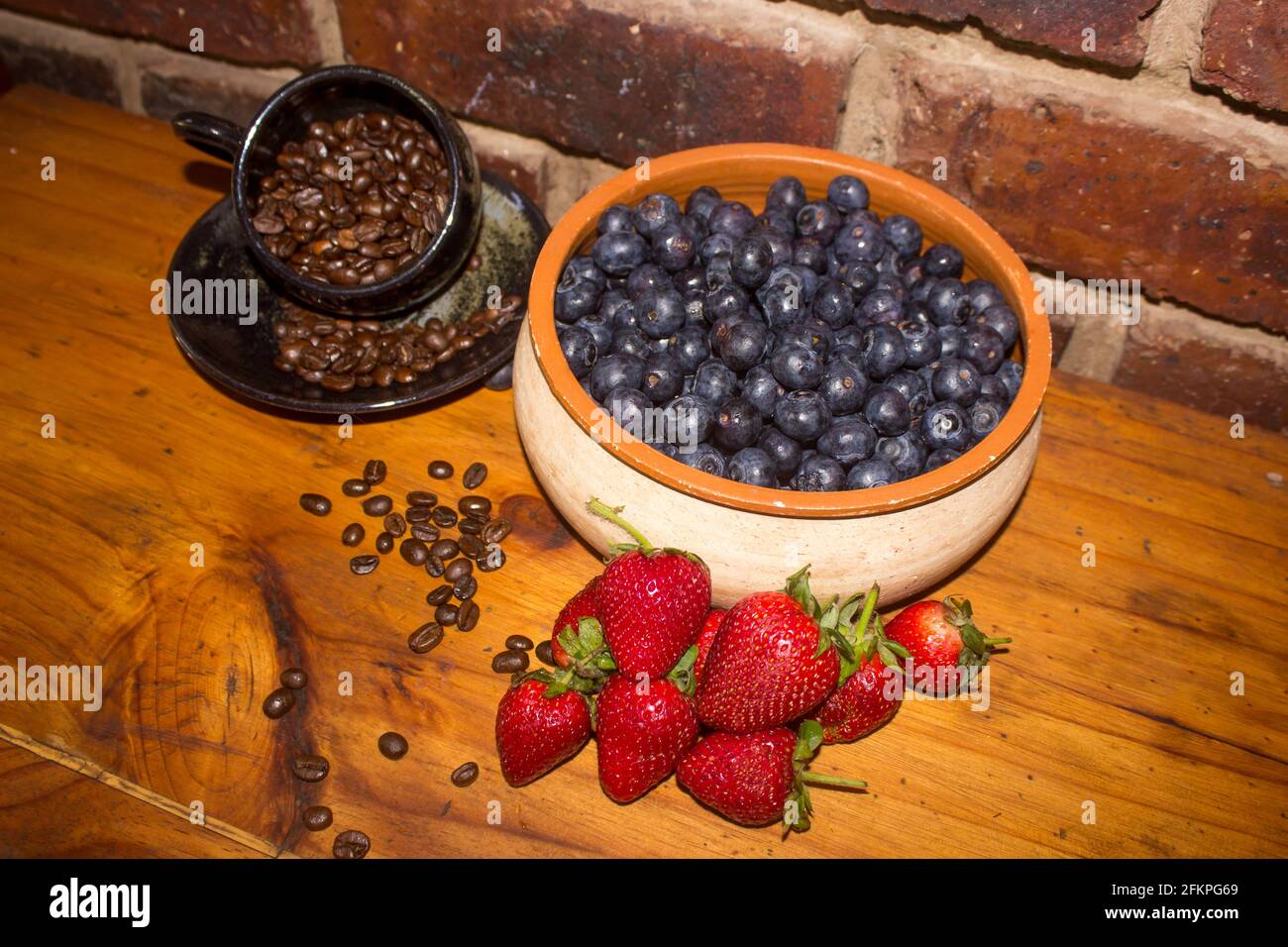 A still live consisting of coffee beans, strawberries and a bowl filled with blueberries, on a wooden tabletop. Stock Photo