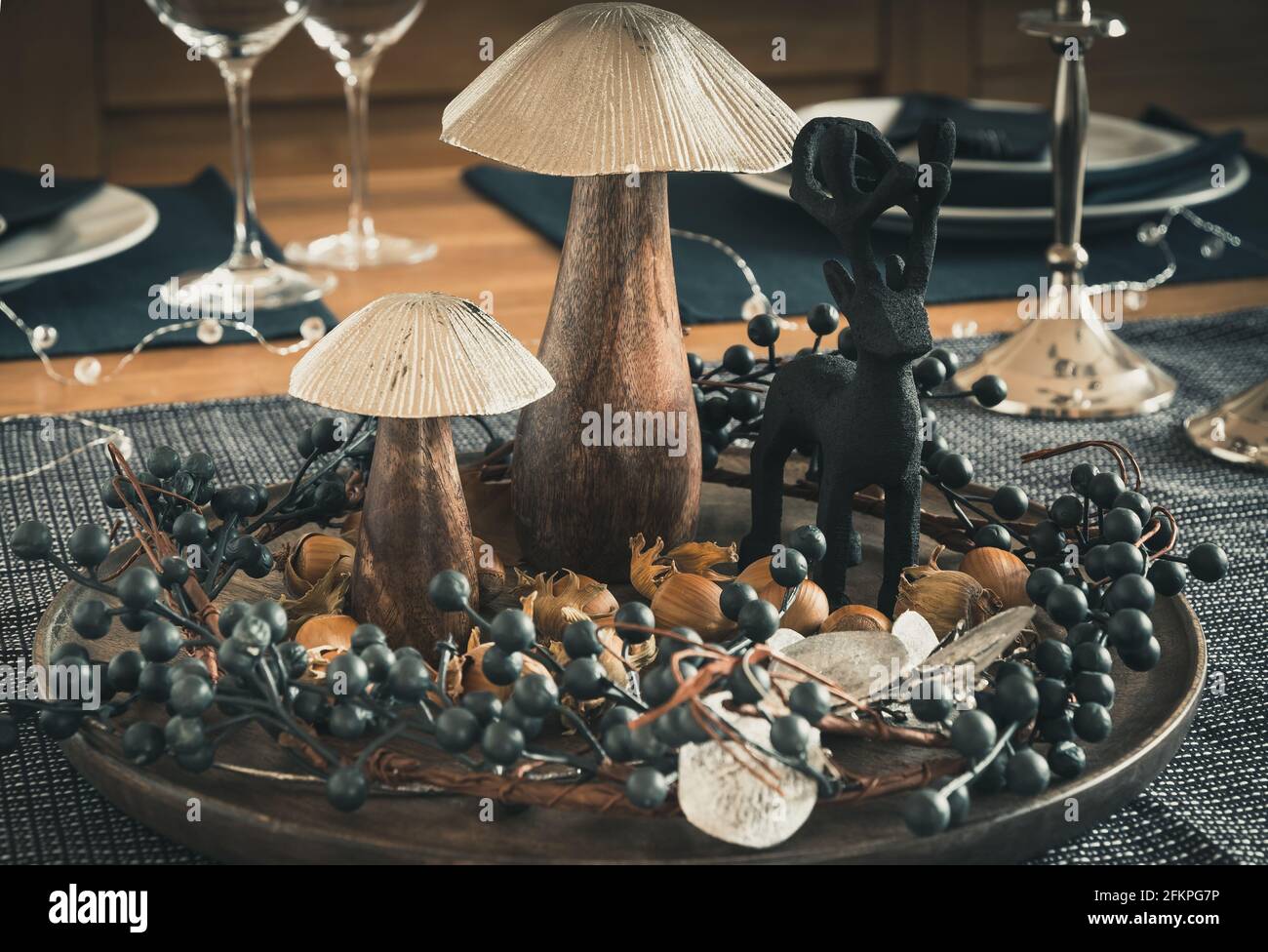 Autumnal table decoration with wooden mushrooms, berry wreath, hazelnuts and a wooden deer, dominated by dark blue, silver and wood colors Stock Photo