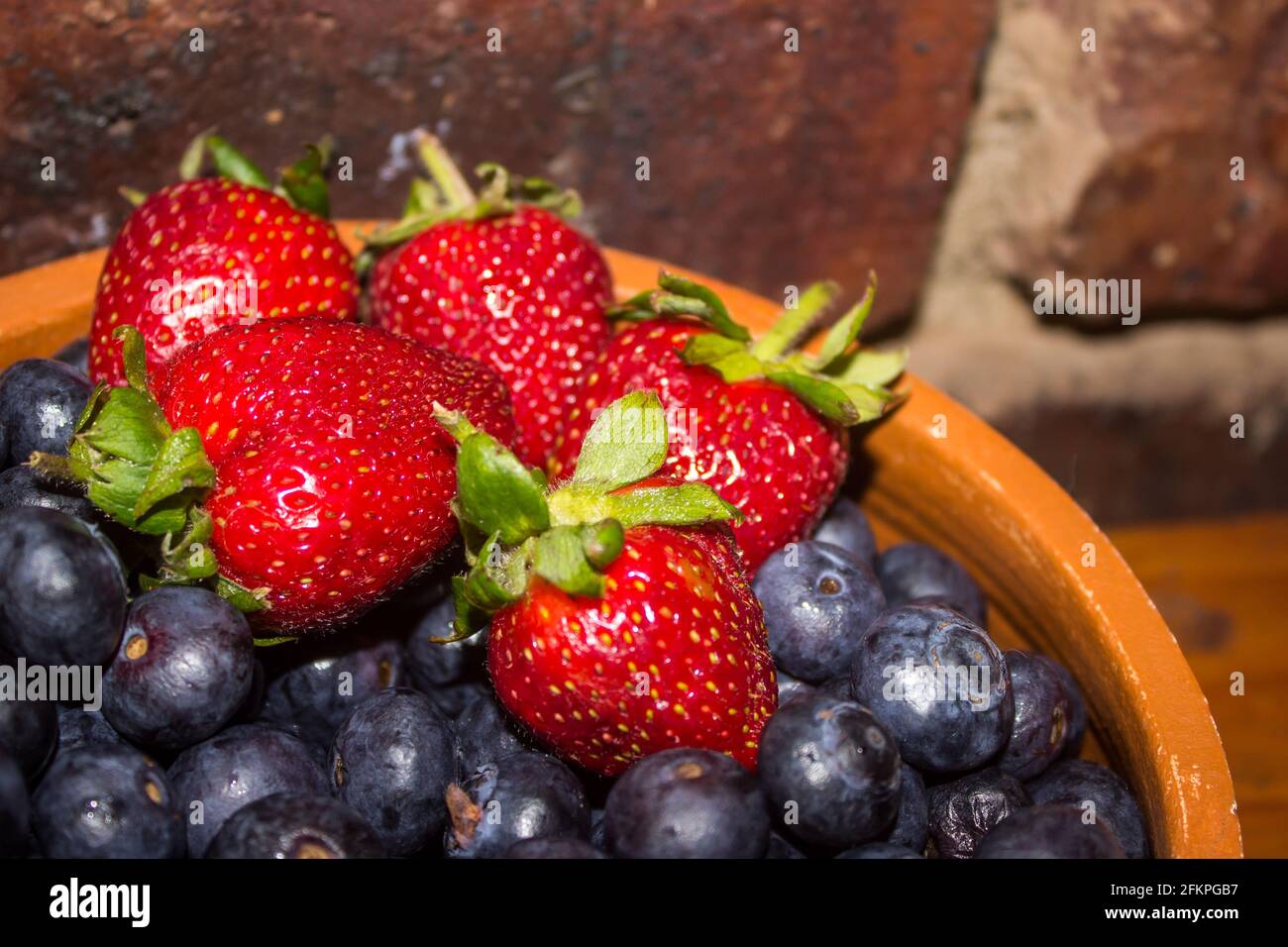 A rustic Bowl with a few bright red strawberries, on top of a large amount of indigo-colored blueberries Stock Photo