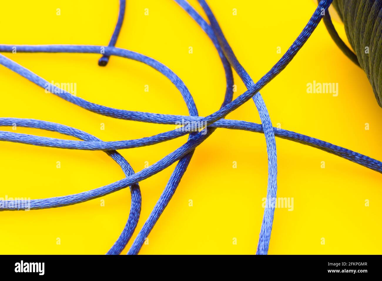 Thin blue string on yellow background, messy thread off the spool without order, jumble of