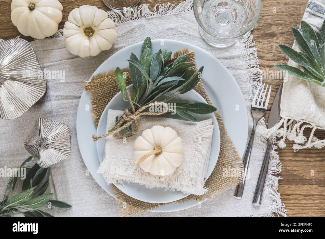 Top view of place setting on a wooden table with white mini pumpkins, sage leaves and crystal glasses for Thanksgiving Day or Halloween Stock Photo