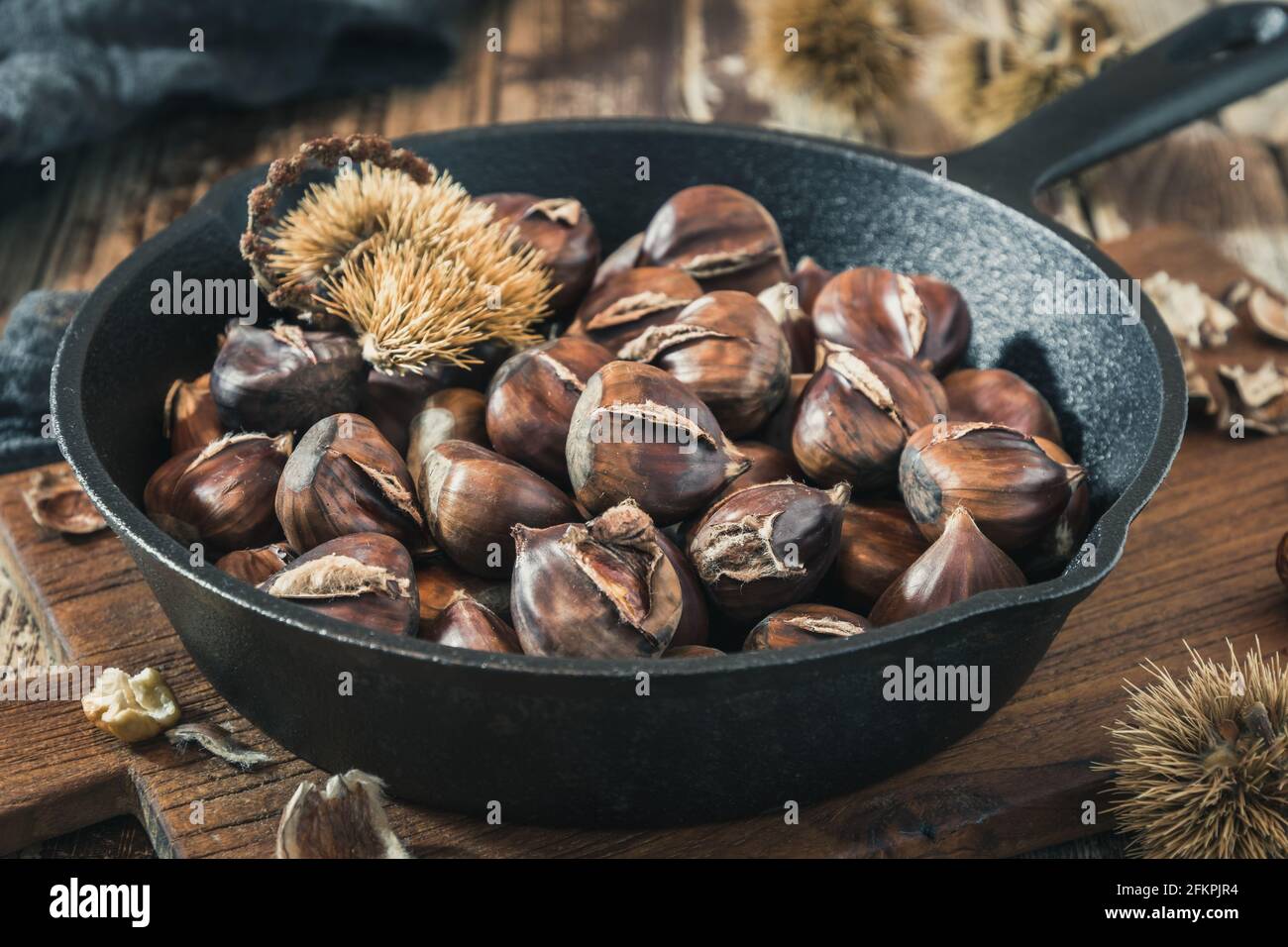 Roasted chestnuts in a cast iron pan on a wooden board Stock Photo