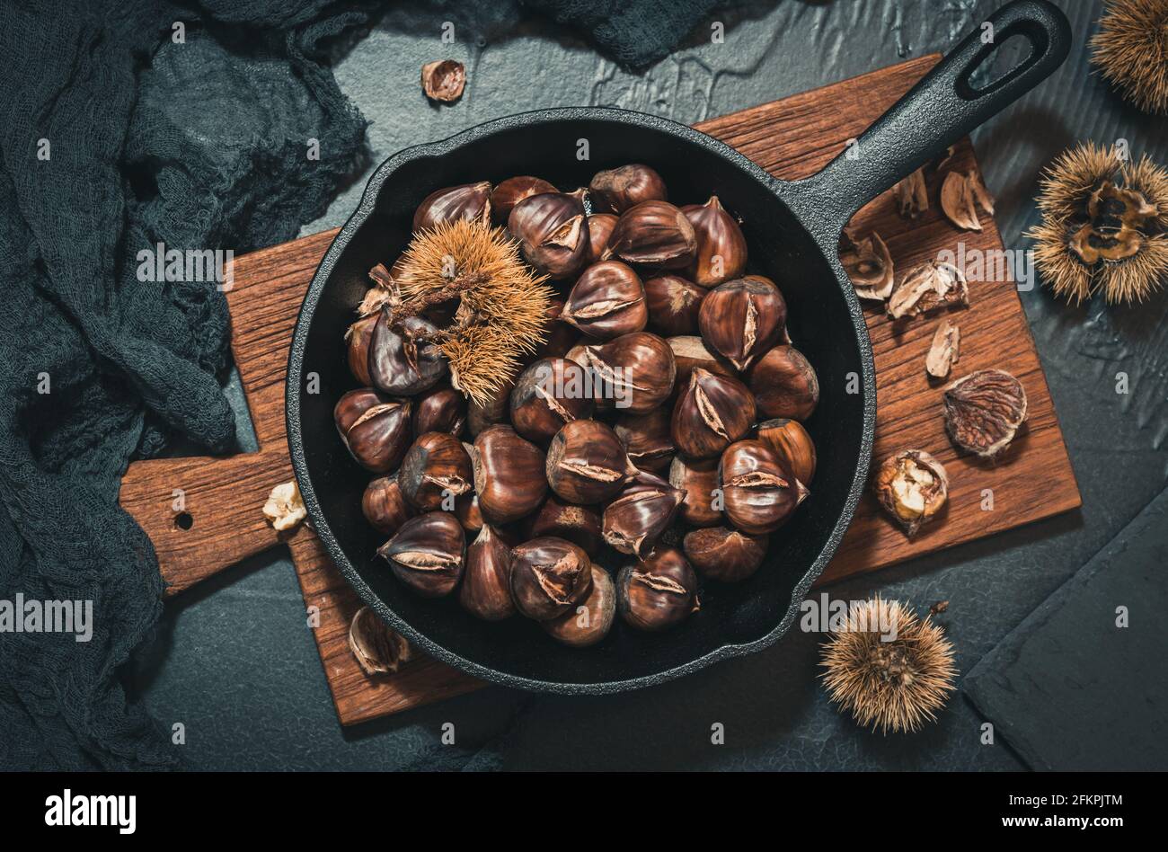 Top view on a cast iron pan with roasted chestnuts on a wooden board on black background Stock Photo