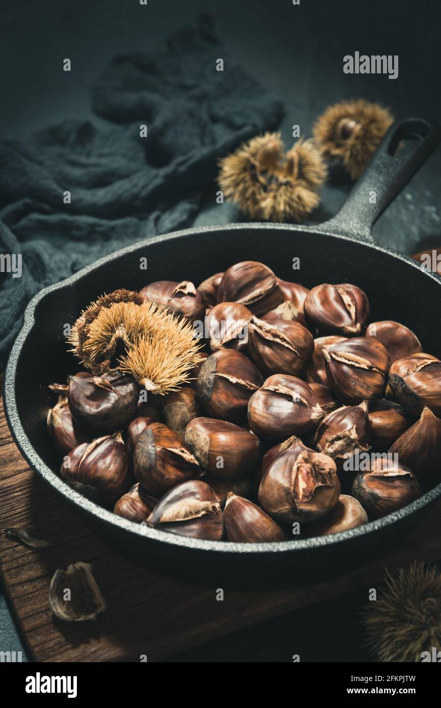 Cast iron pan with roasted chestnuts on a black background, vertical stock photo. Stock Photo