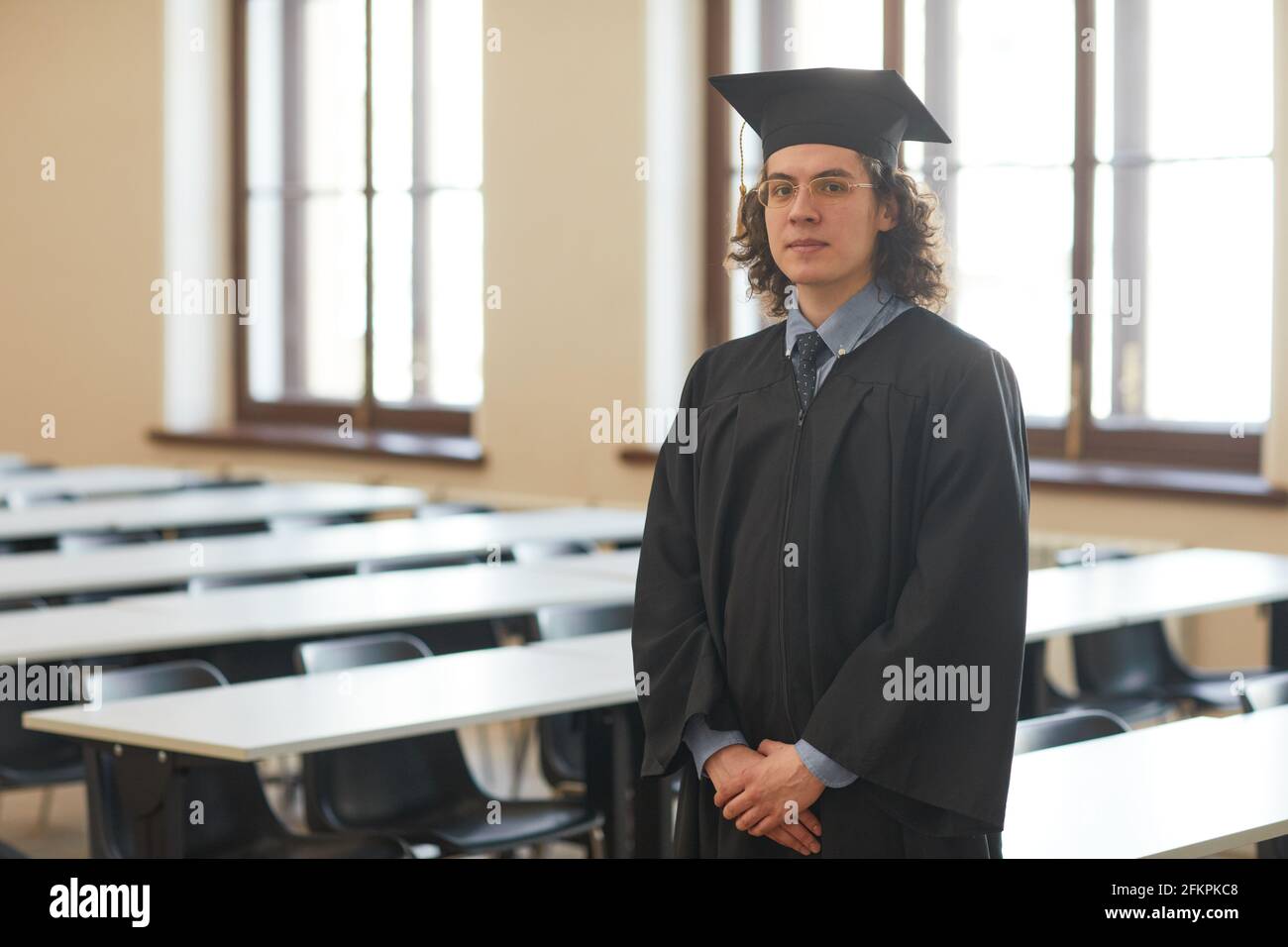 Waist up portrait of young man wearing graduation robe and looking at ...