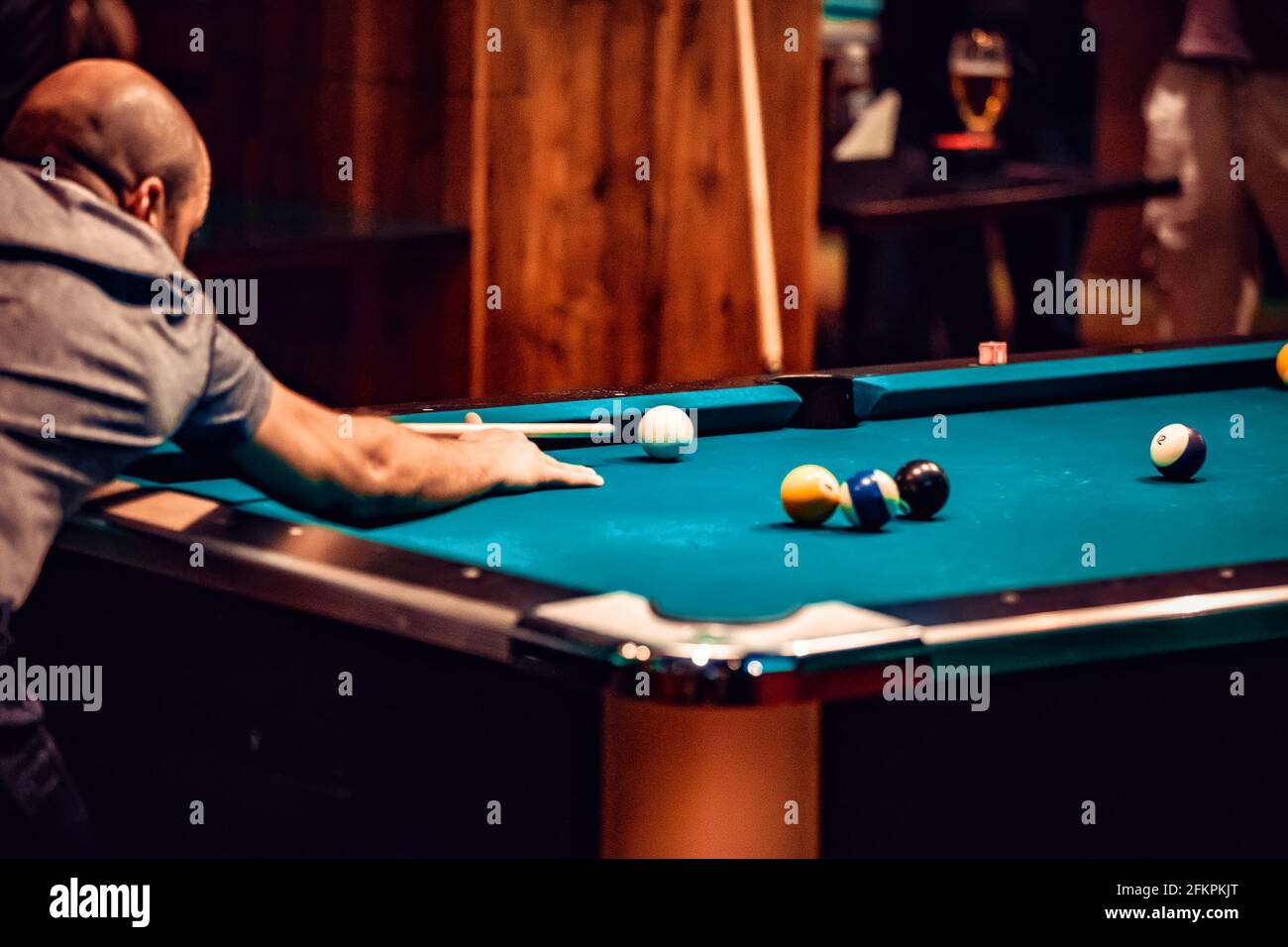 Man playing snooker, bent over to hit white ball on pool billiards table.  Stock Photo