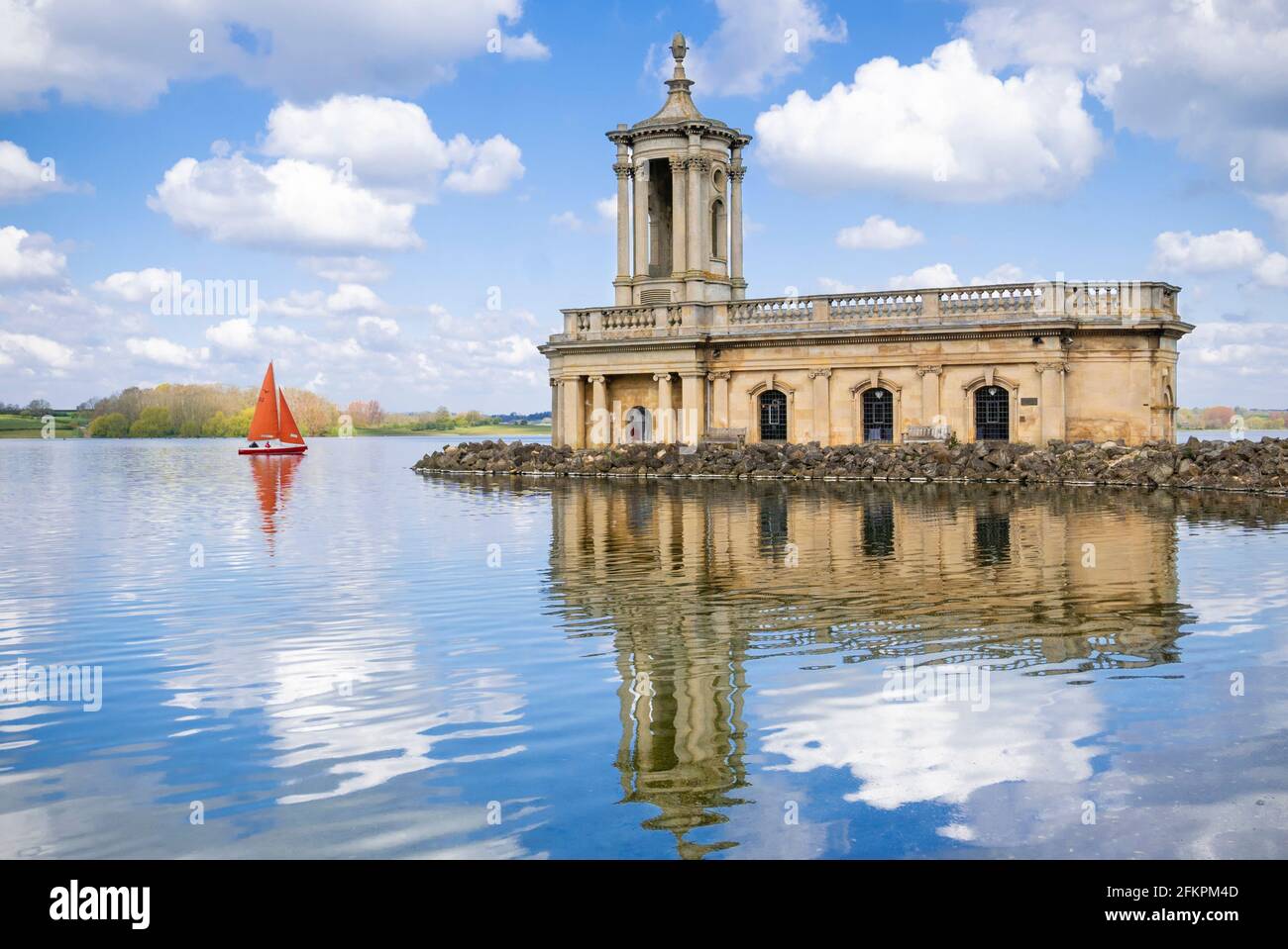 One Sailing boat or One yacht with red sails sailing past Normanton Church Rutland water reservoir Oakham Rutland England UK GB Europe Stock Photo