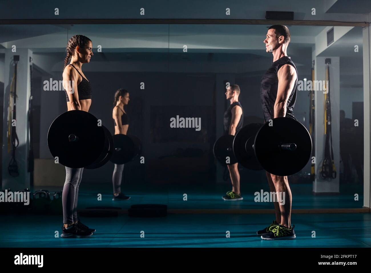 A female and a male training together and simultaneously doing dead-lift exercise at the gym. Stock Photo