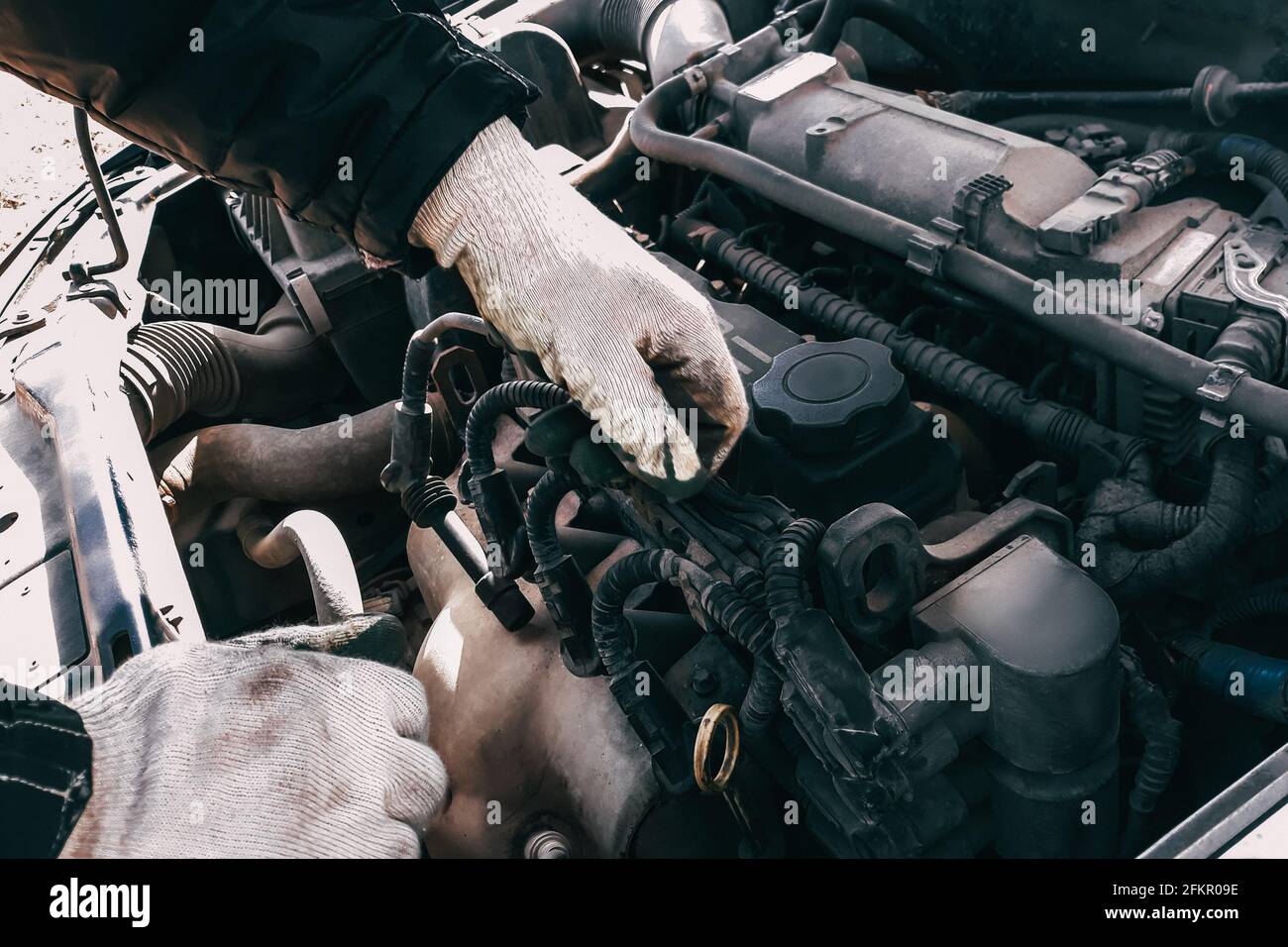 Auto mechanic repairs a car engine. Man's hands in work gloves close-up. Diagnostics and restoration of old parts. Replacement of high-voltage wires. Stock Photo