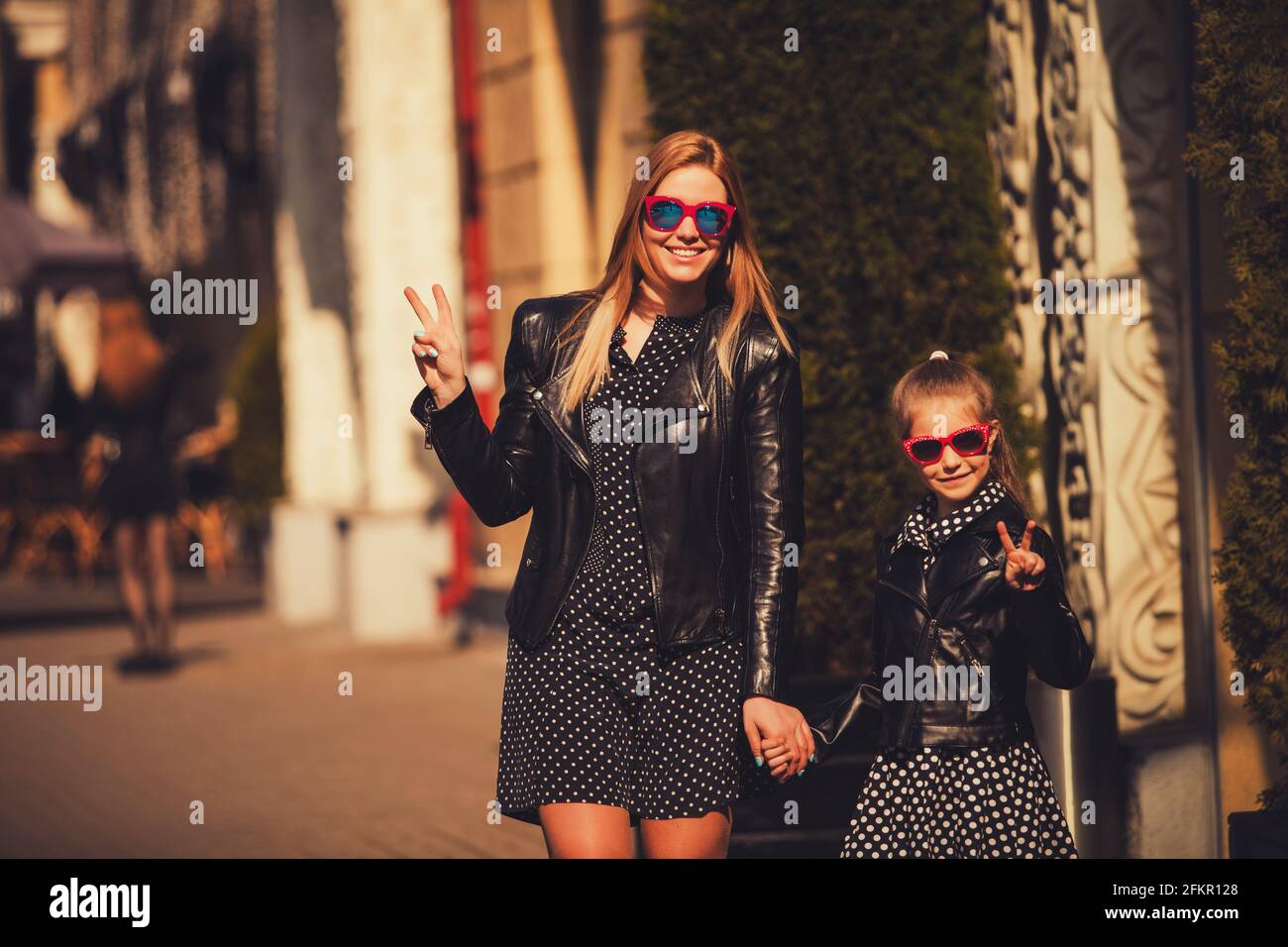 Fashion mom and daughter in leather jackets and gesturing with two fingers Stock Photo