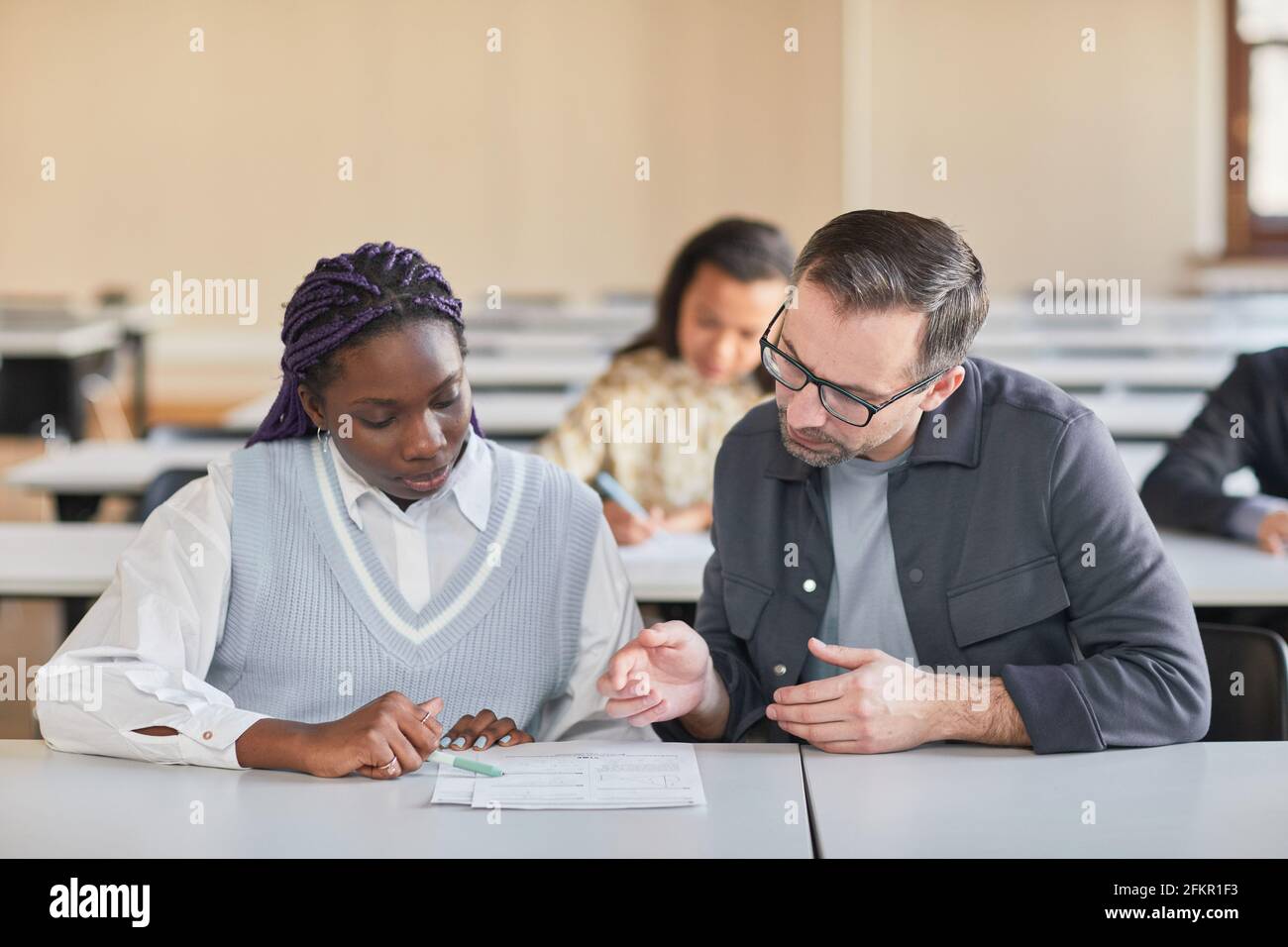 Portrait of mature professor helping African-American woman studying in college auditorium, copy space Stock Photo