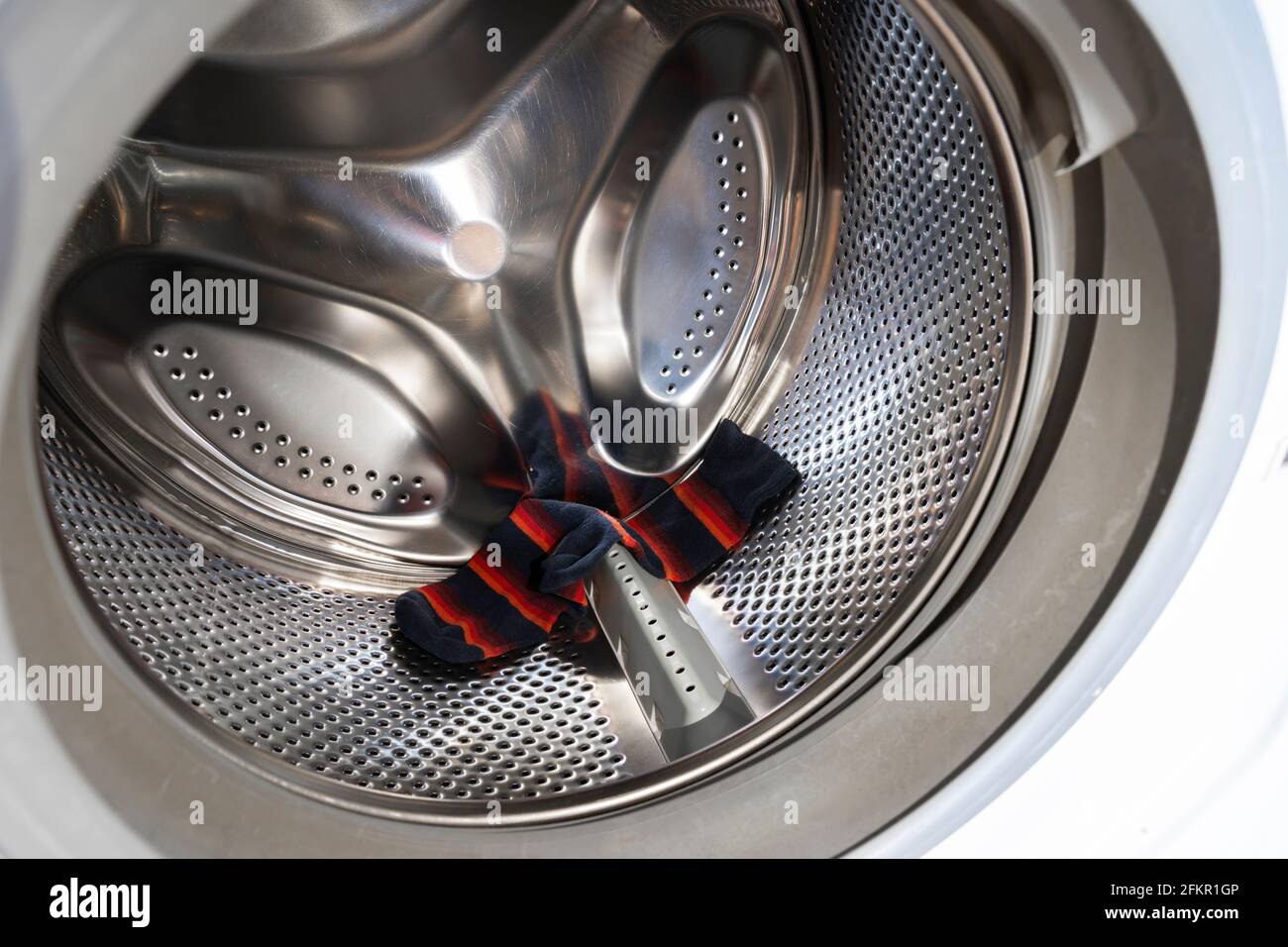 A single red striped sock in a washing machine laundry drum. Concept: the sock monster, sock fairy, hungry washing machine, supernatural cause Stock Photo