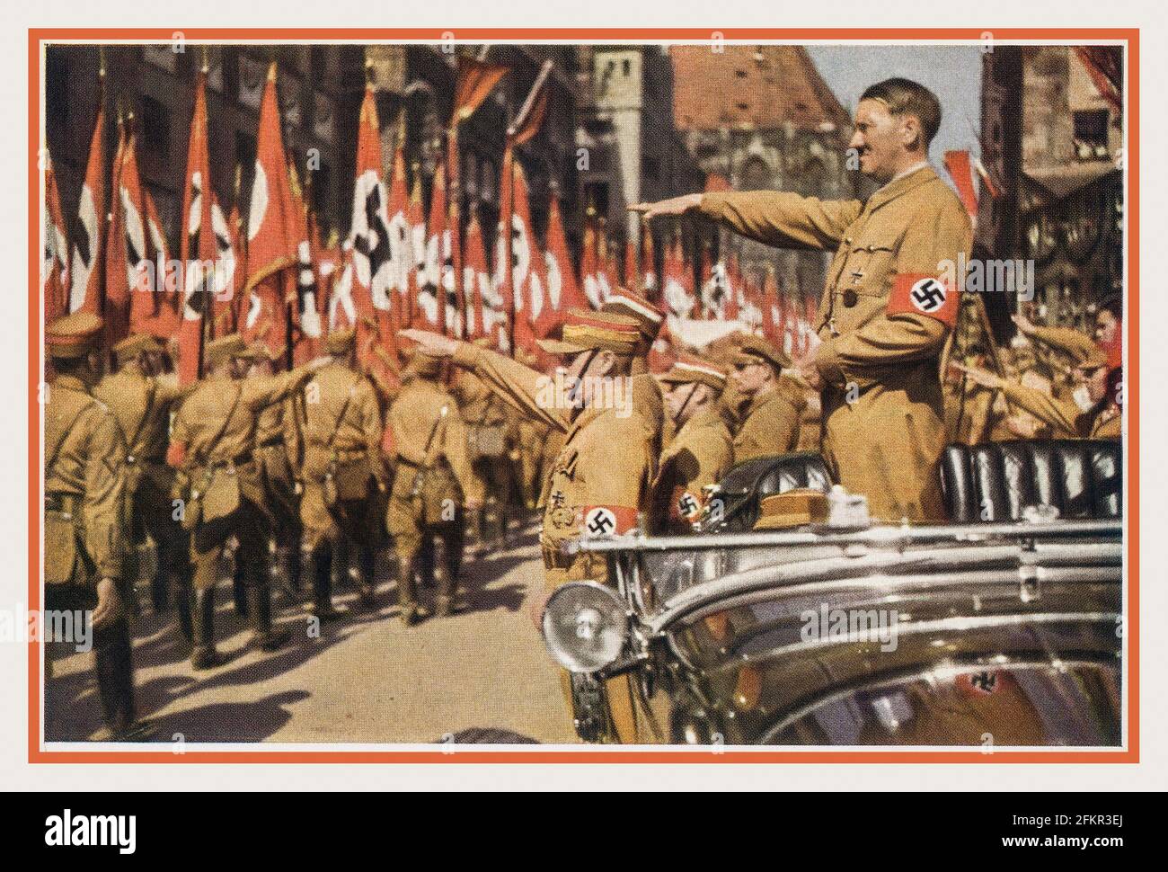 Adolf Hitler saluting SA Troops  Vintage Nazi Germany c1935. Nuremberg Rally, color photo card of Adolf Hitler wearing a swastika armband in open top Mercedes and SA troops marching past with swastika flags, Verlag H. Wiedemann ,Sturmabteilung The official uniform of the SA was the brown shirt with a brown tie  'The Brown Shirts'. Stock Photo