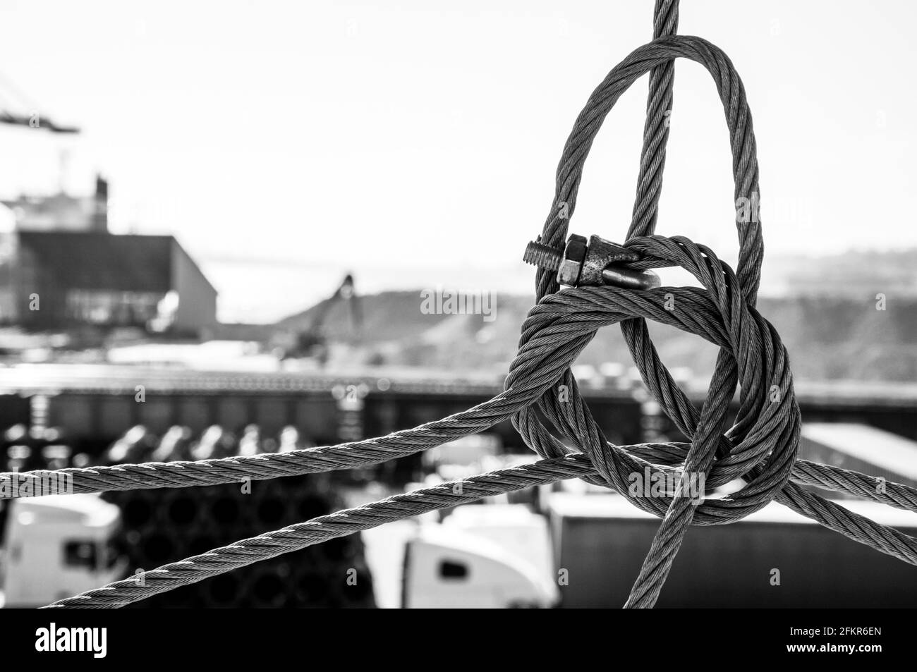 Black and white photo of wire rope knot closeup with blurred industrial landscape on background. TIS cargo terminal in port of Ukraine. Industrial bac Stock Photo