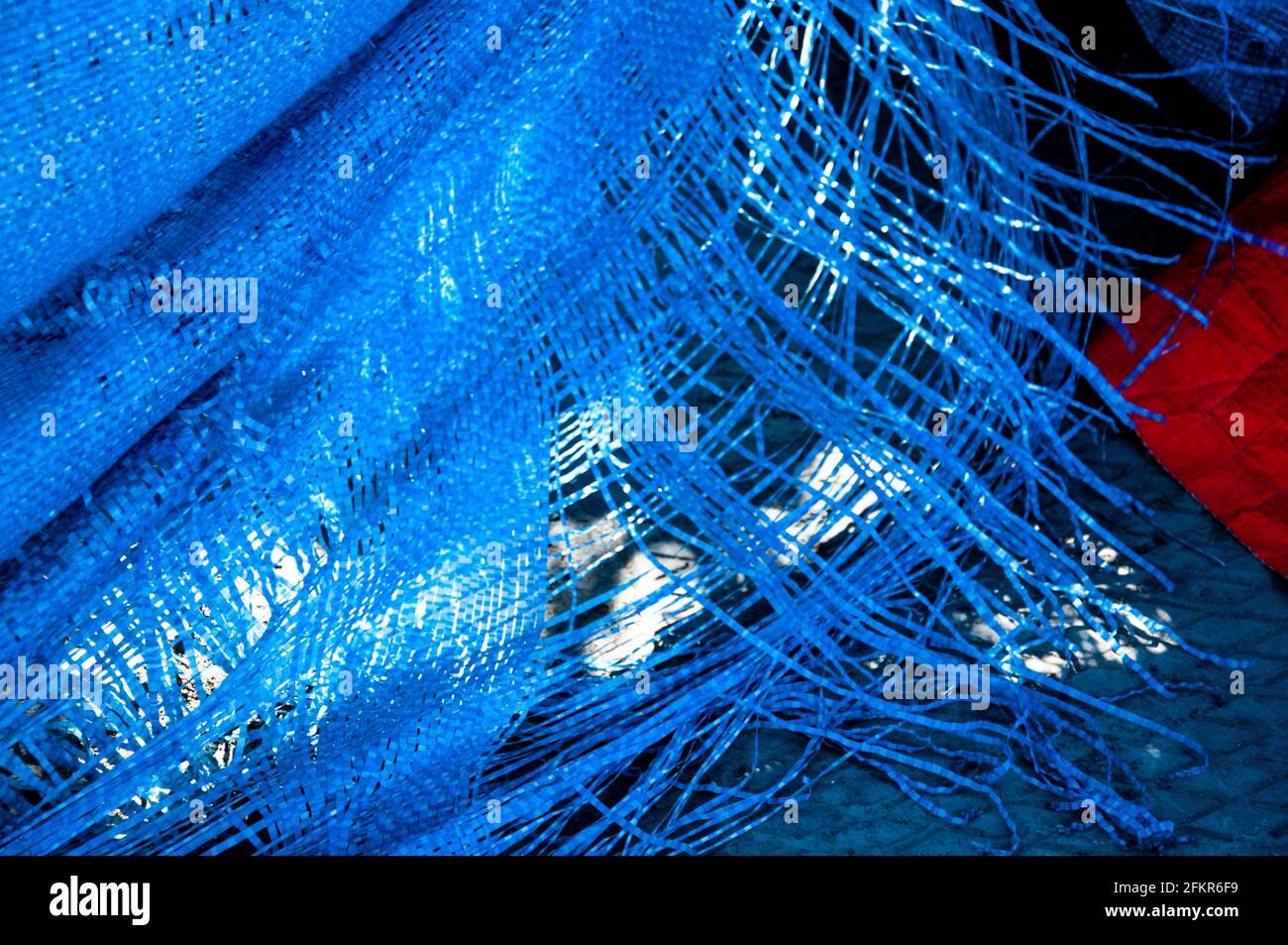 Bright blue color plastic industrial fabric with textured ragged edges. Torn wrap with long fringed fibers. Blue and red backdrop. Grunge texture. Ind Stock Photo