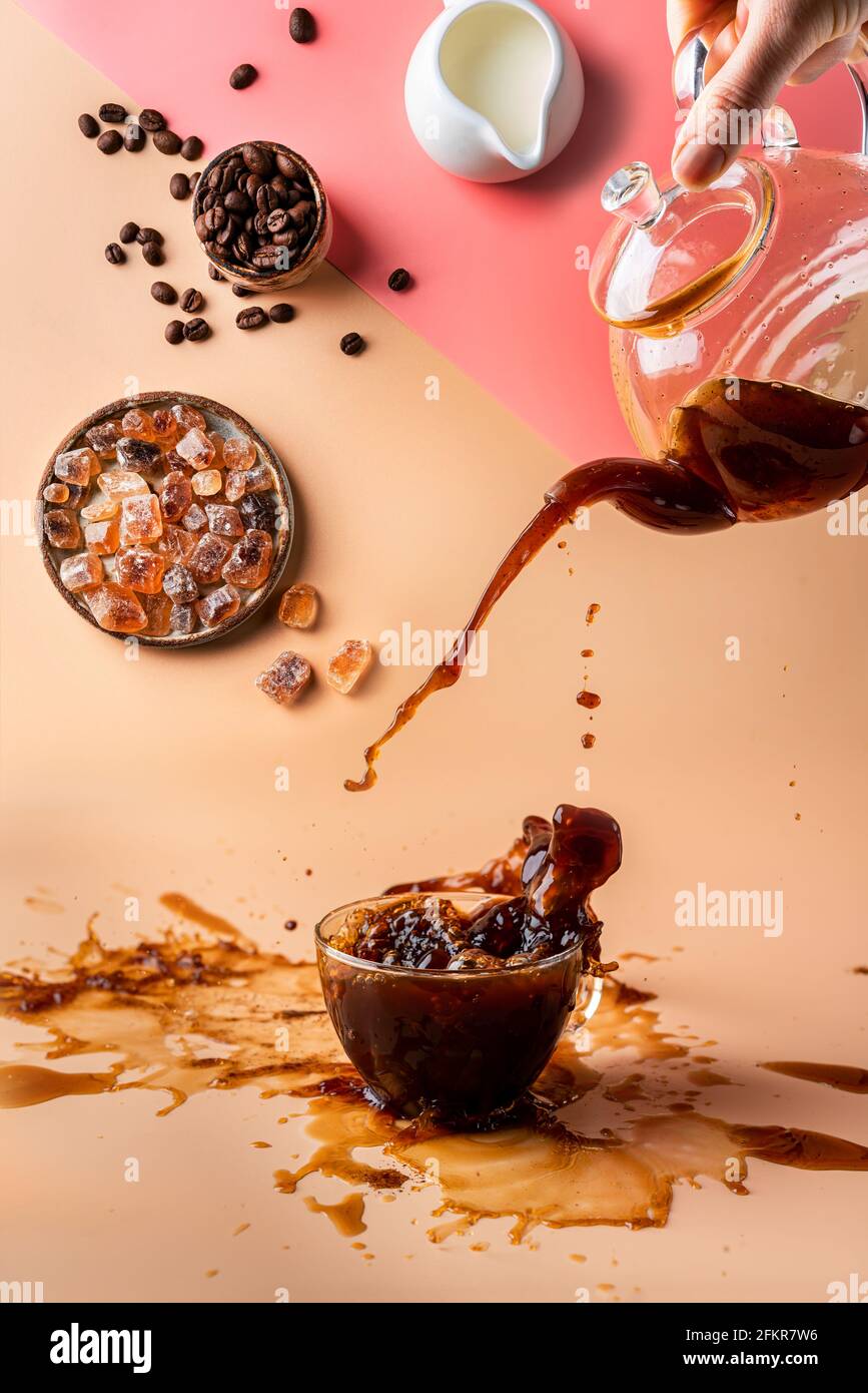 pouring coffee in a cup creating splashes with ingredients on colorful orange and pink background Stock Photo