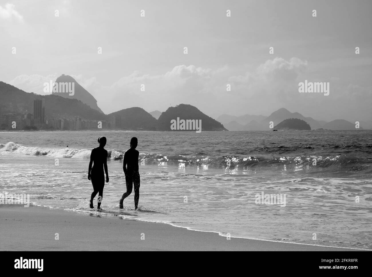 Silhouette of two young women walking on the sandy beach in monochrome Stock Photo