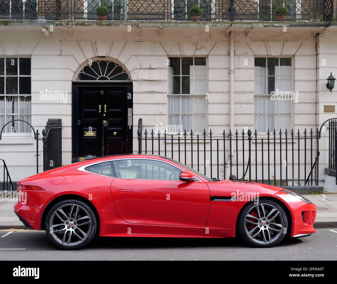 London, Greater London, England - Apr 27 2021: Red sportscar parked outside a residential property with railings and balcony. Stock Photo