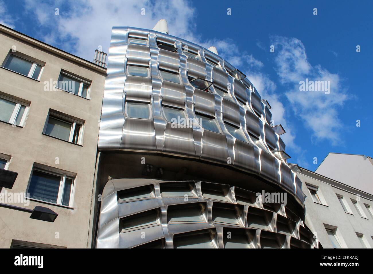 Futuristic metal curved building inbetween two typical buildings. Branch Bank Building in Vienna, Austria. Smashed Building Stock Photo