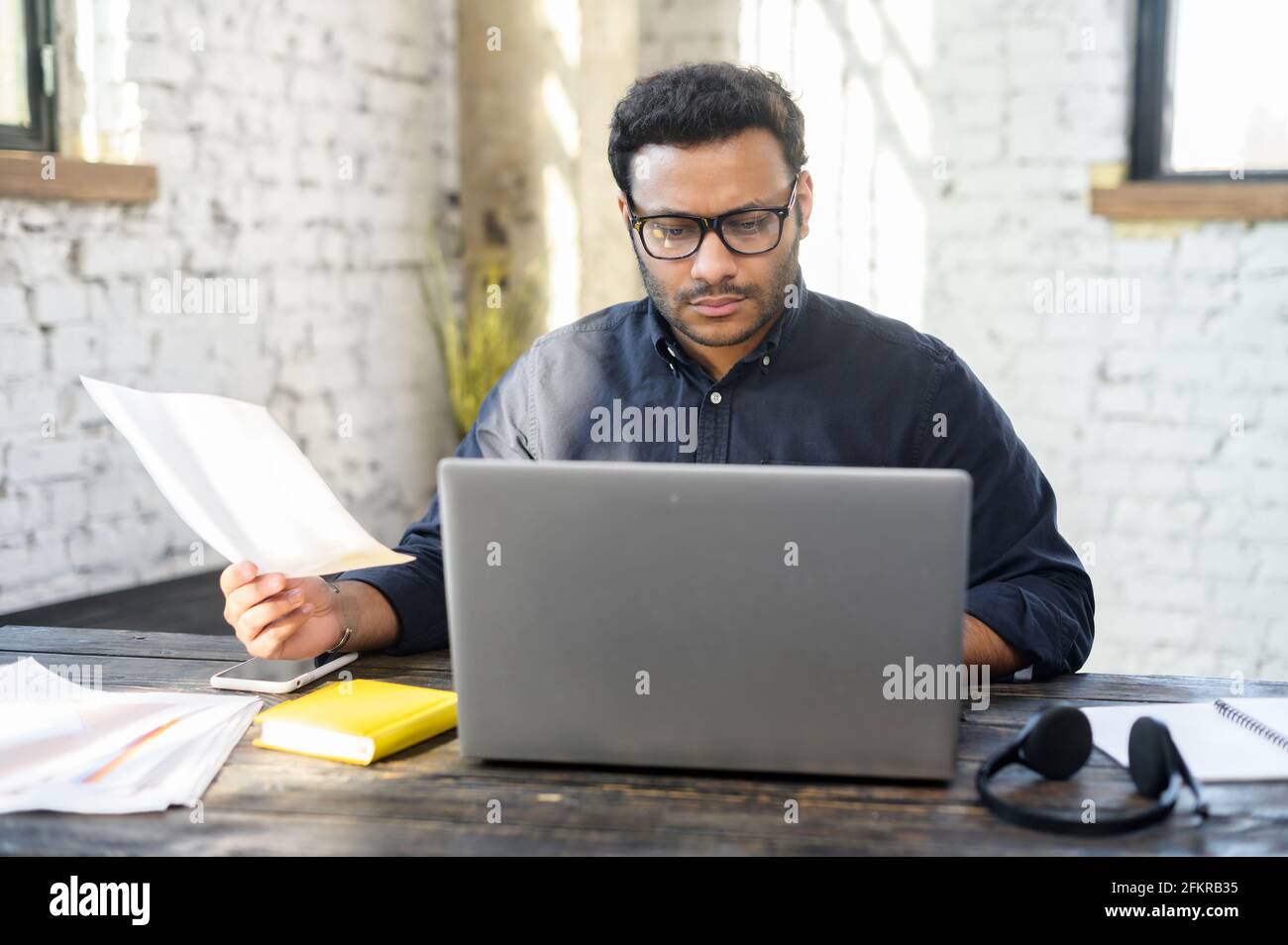 https://c8.alamy.com/comp/2FKRB35/executive-mixed-race-male-office-employee-doing-paperwork-sitting-at-the-desk-with-laptop-in-office-focused-and-serious-hindu-man-in-smart-casual-looking-through-sheets-of-documents-preparing-report-2FKRB35.jpg