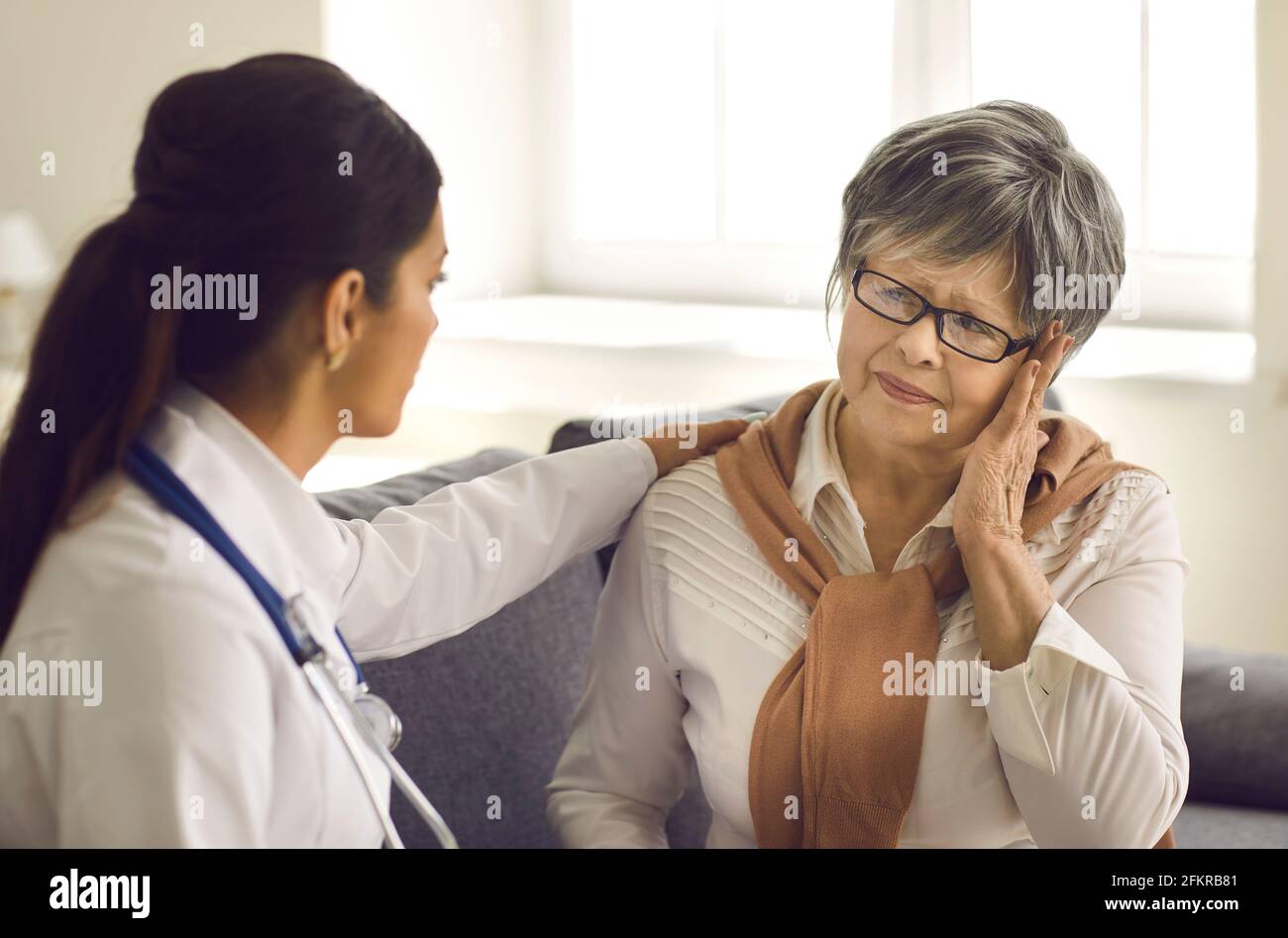 Mature woman telling doctor about her headaches during health checkup at hospital Stock Photo