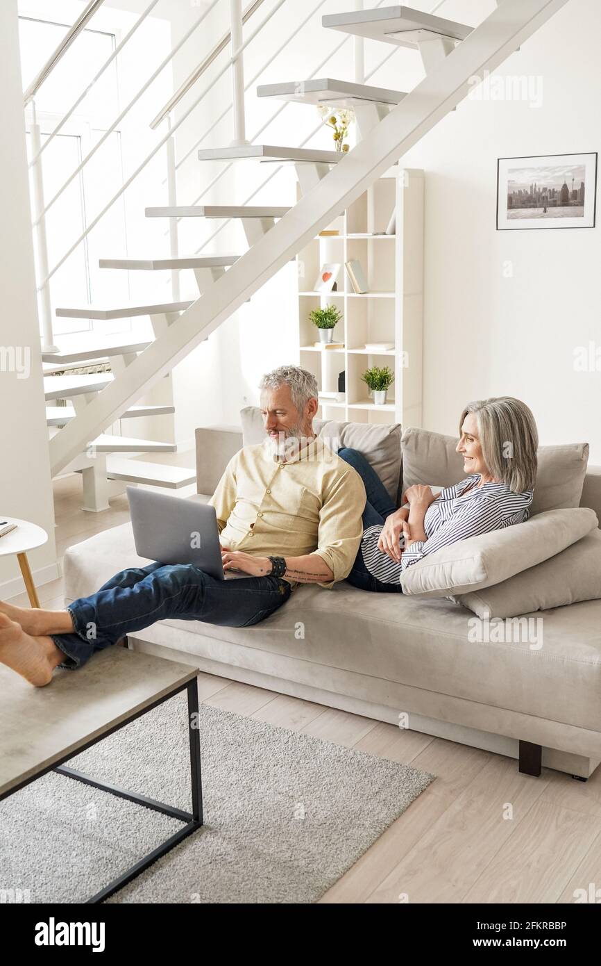 Happy mature senior couple using devices relaxing at home on sofa. Stock Photo