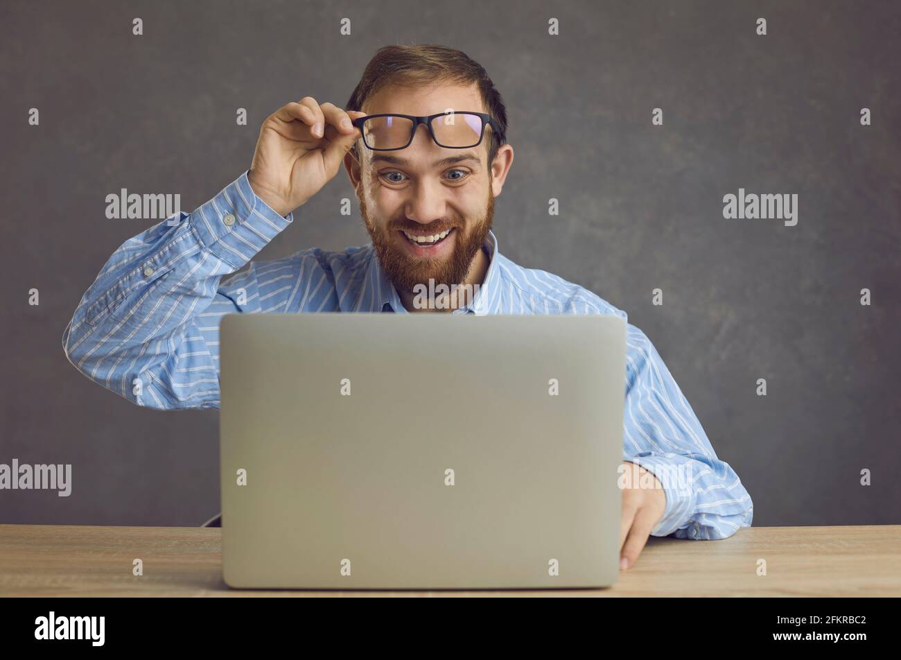 Happy surprised business man takes off glasses looking at screen of laptop computer Stock Photo