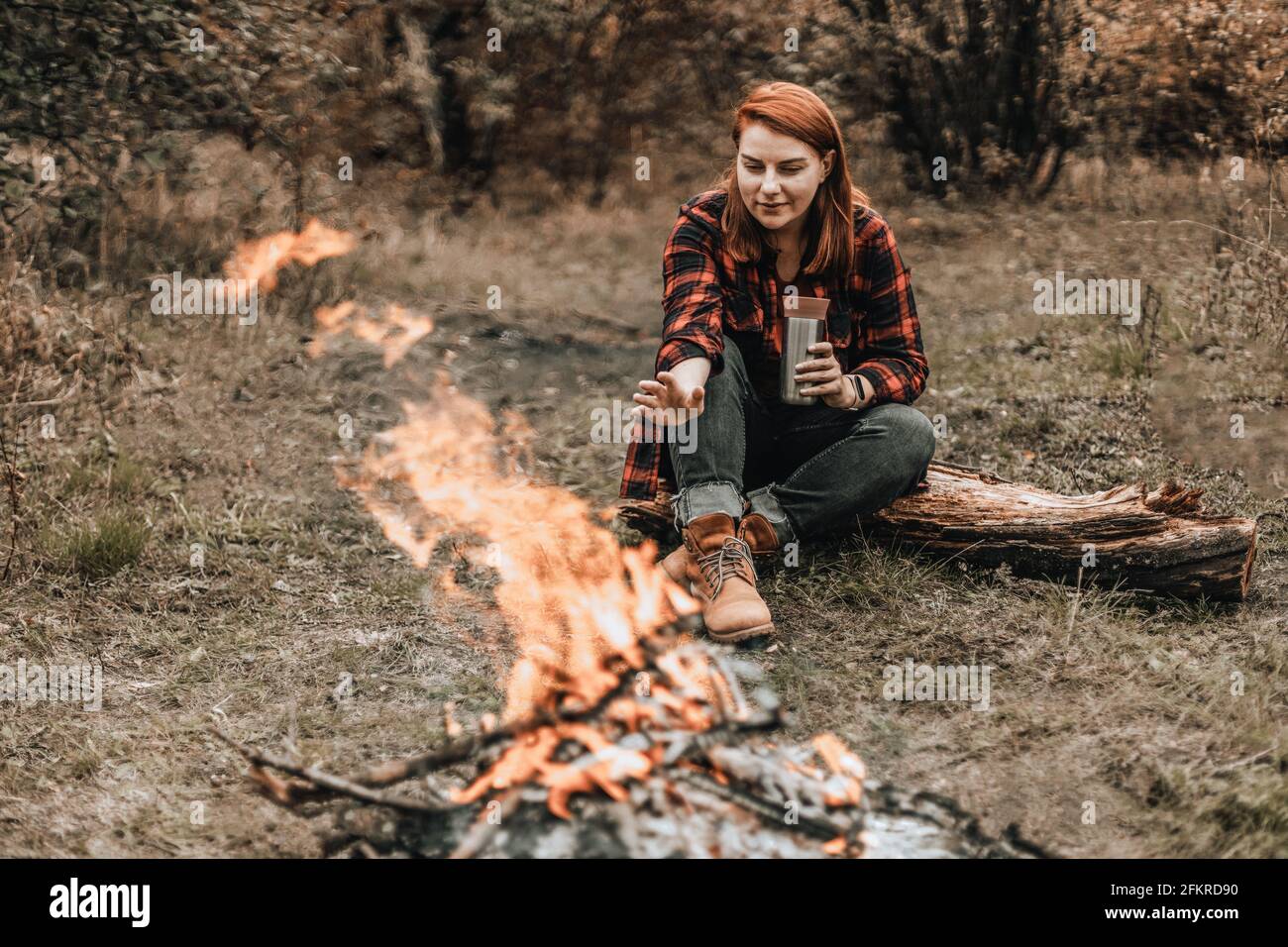 Traveler woman camping in the forest and relaxing near campfire after a very hard day. Concept of trekking, adventure and seasonal vacation. Stock Photo