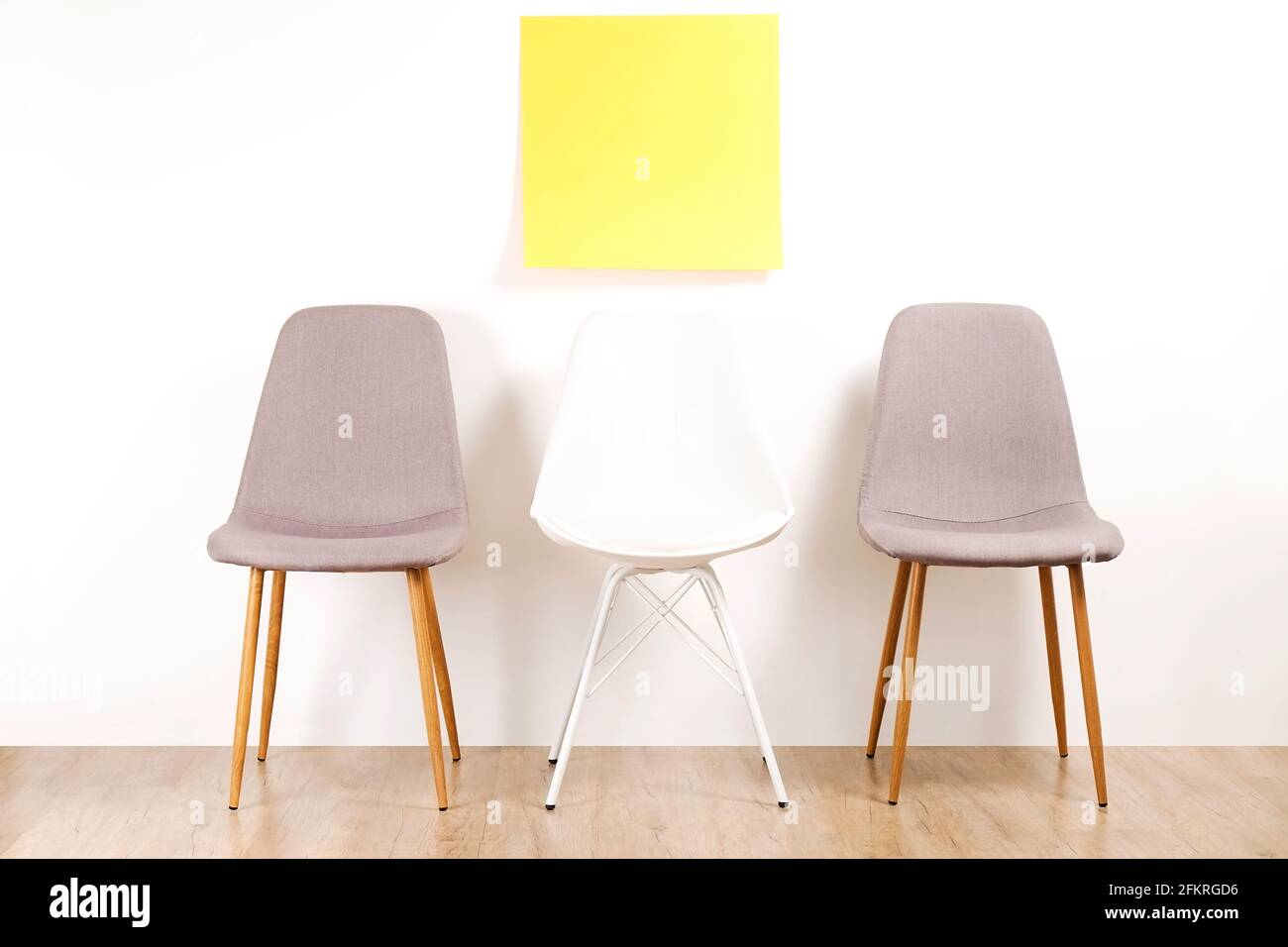 Three empty available loft style chair seats on wooden floor with blank ad poster, white wall background, yellow copy space sticker for text. Intervie Stock Photo