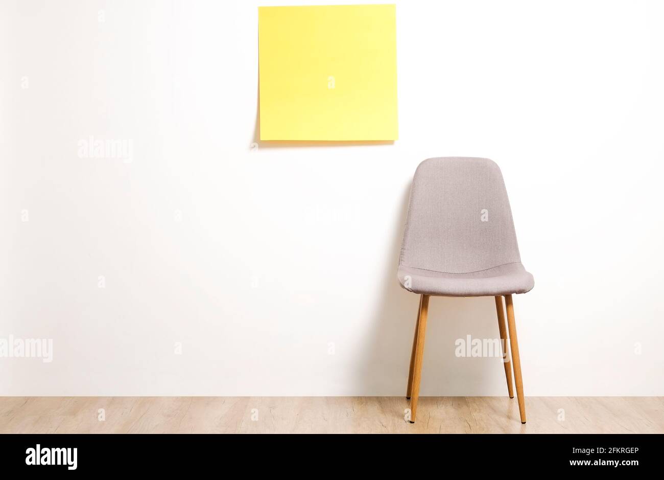 Single empty loft style gray chair on wooden floor, blank ad poster and white wall background, yellow sticker with copy space for your text. Interview Stock Photo