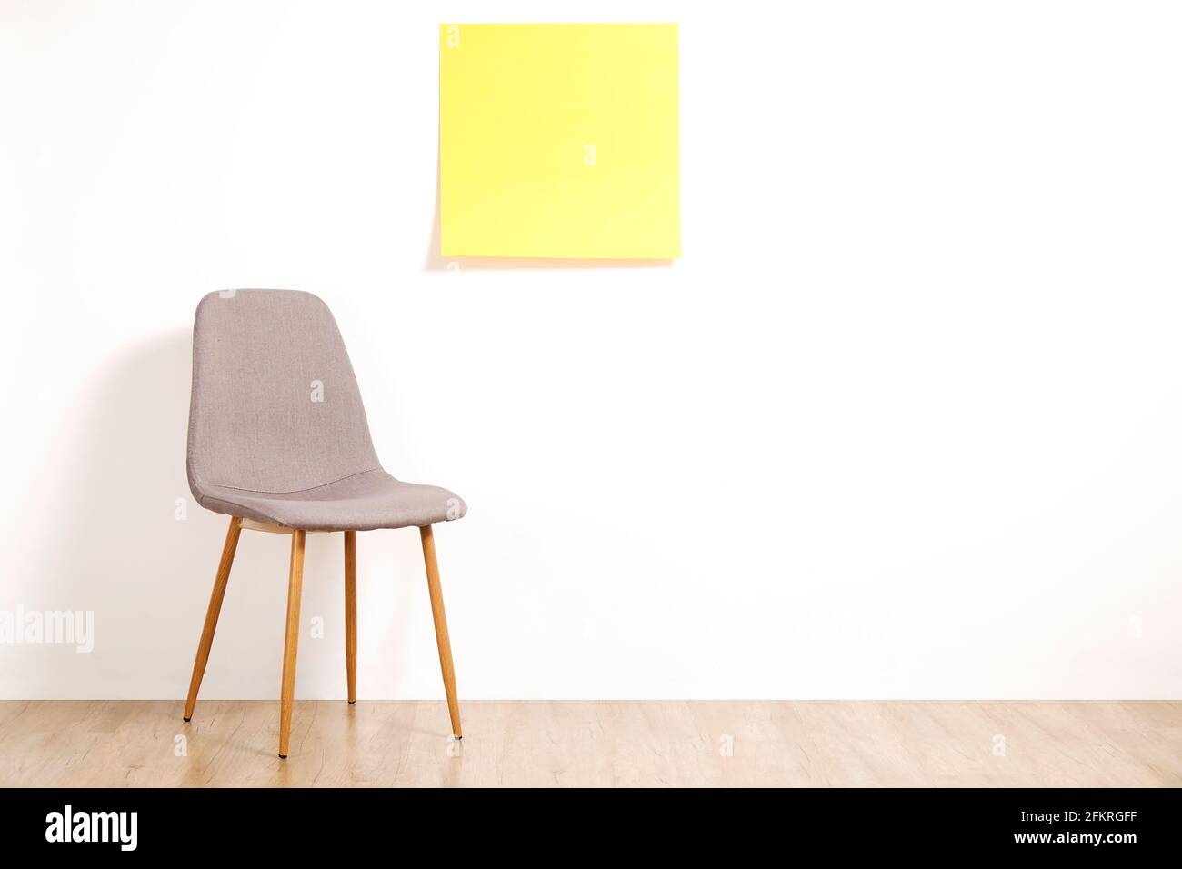 Single empty loft style gray chair on wooden floor, blank ad poster and white wall background, yellow sticker with copy space for your text. Interview Stock Photo