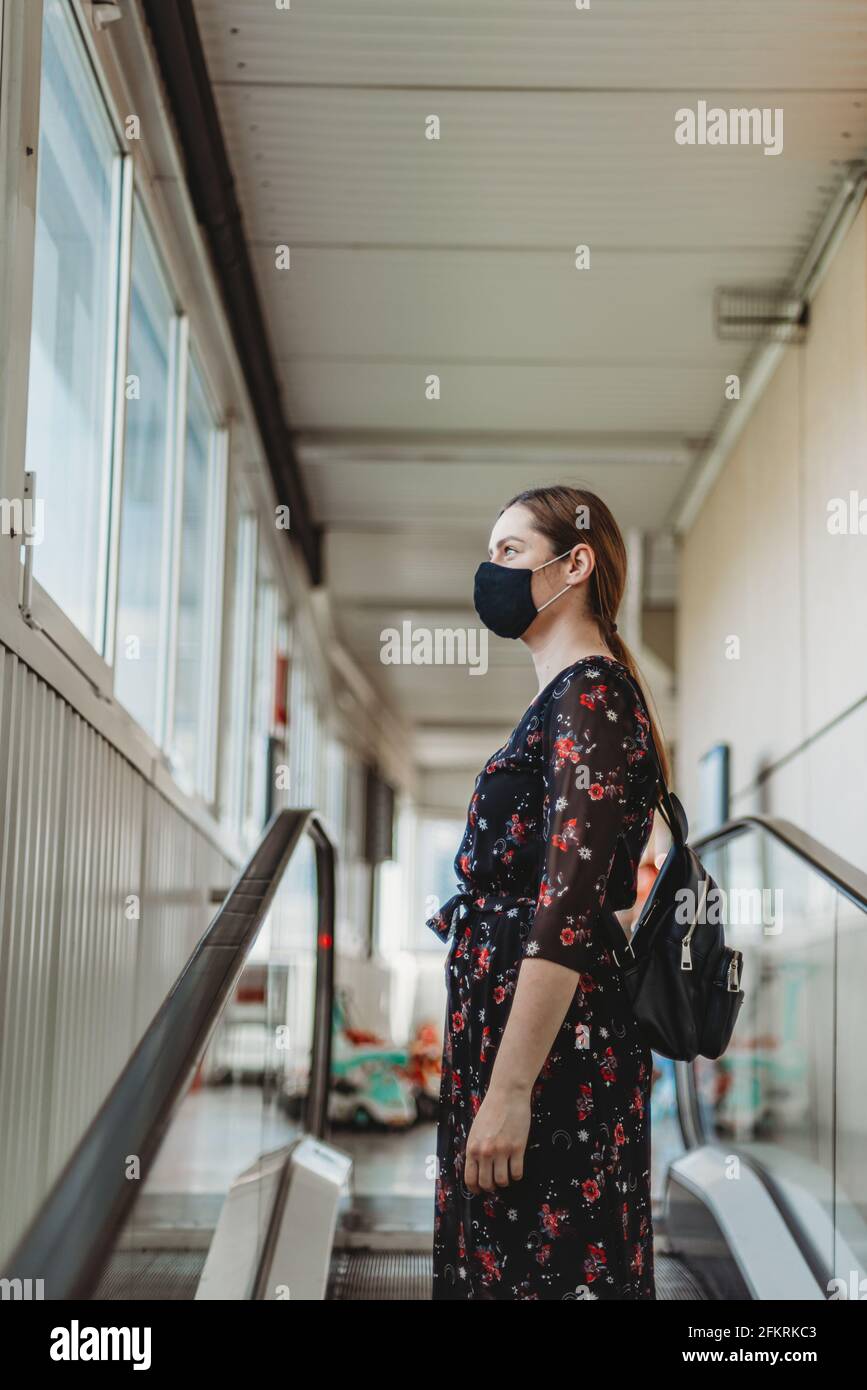 woman with face mask standing on moving escalator Stock Photo