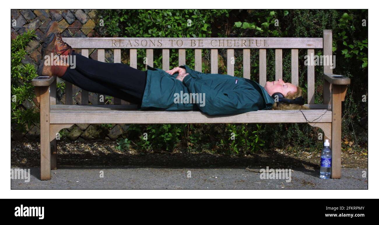 A memorial bench to Ian Dury in poets corner, Pembrook Lodge, Richmond park. Jane Mills enjoys the sun and the music of Dury by pluging her headphones into sockets in the arm rests of this special bench.pic David Sandison 29/4/2002 Stock Photo