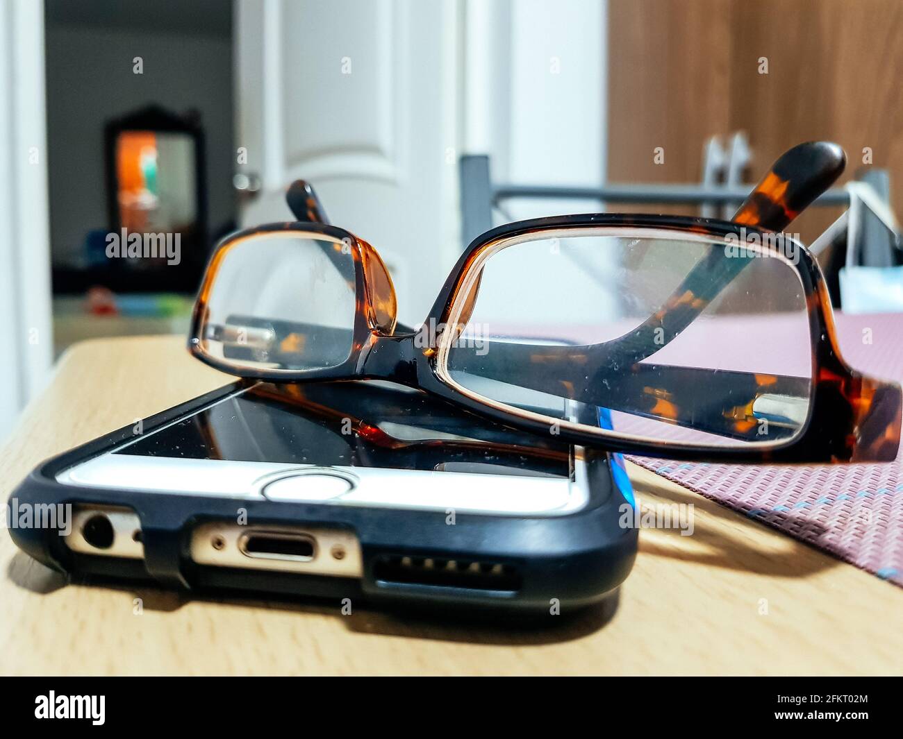 Eyeglasses with mobile phone on wooden table at night, close up Stock