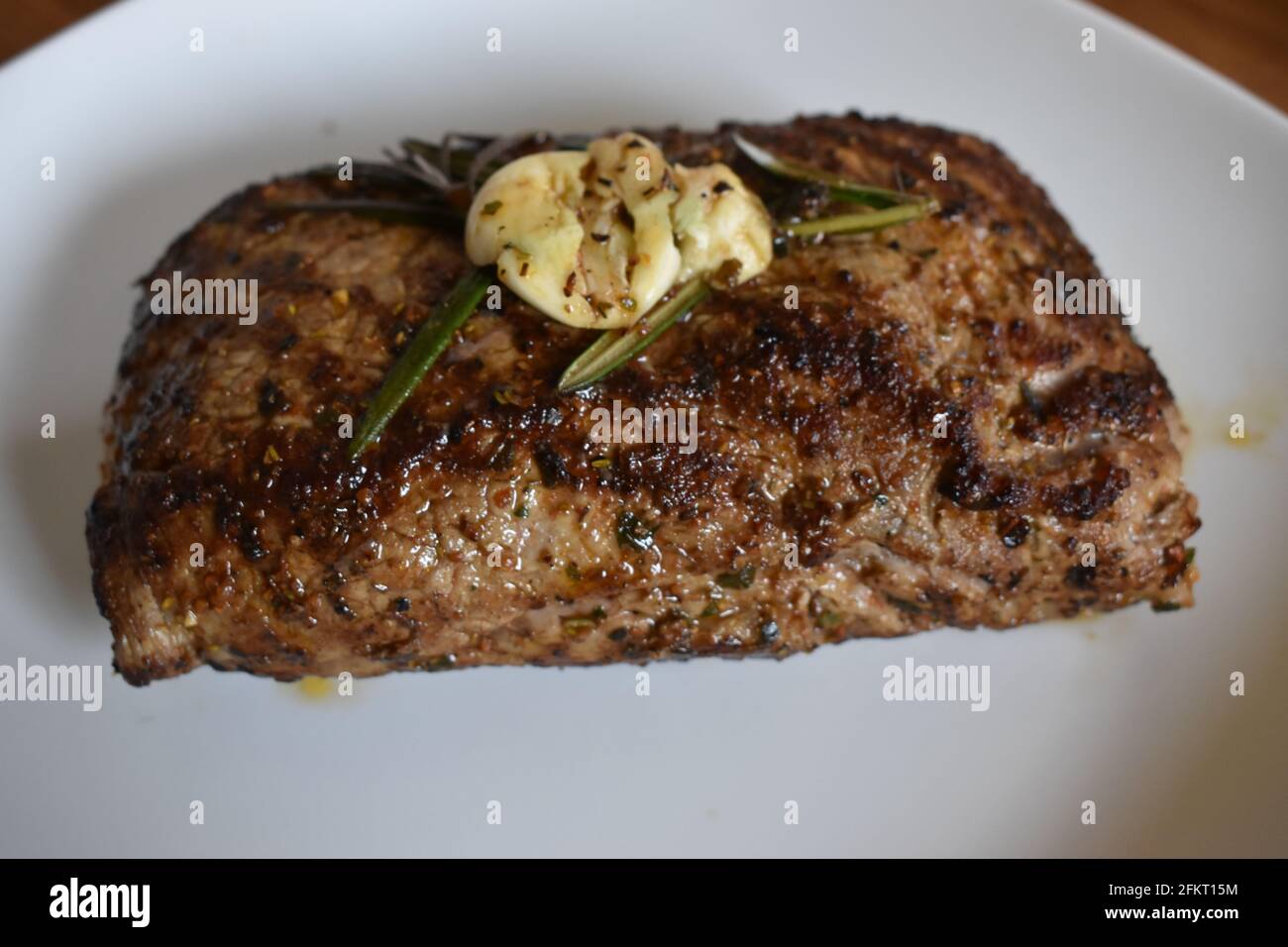 Closeup shot of newly cooked steak topped with herbs on a white plate Stock Photo